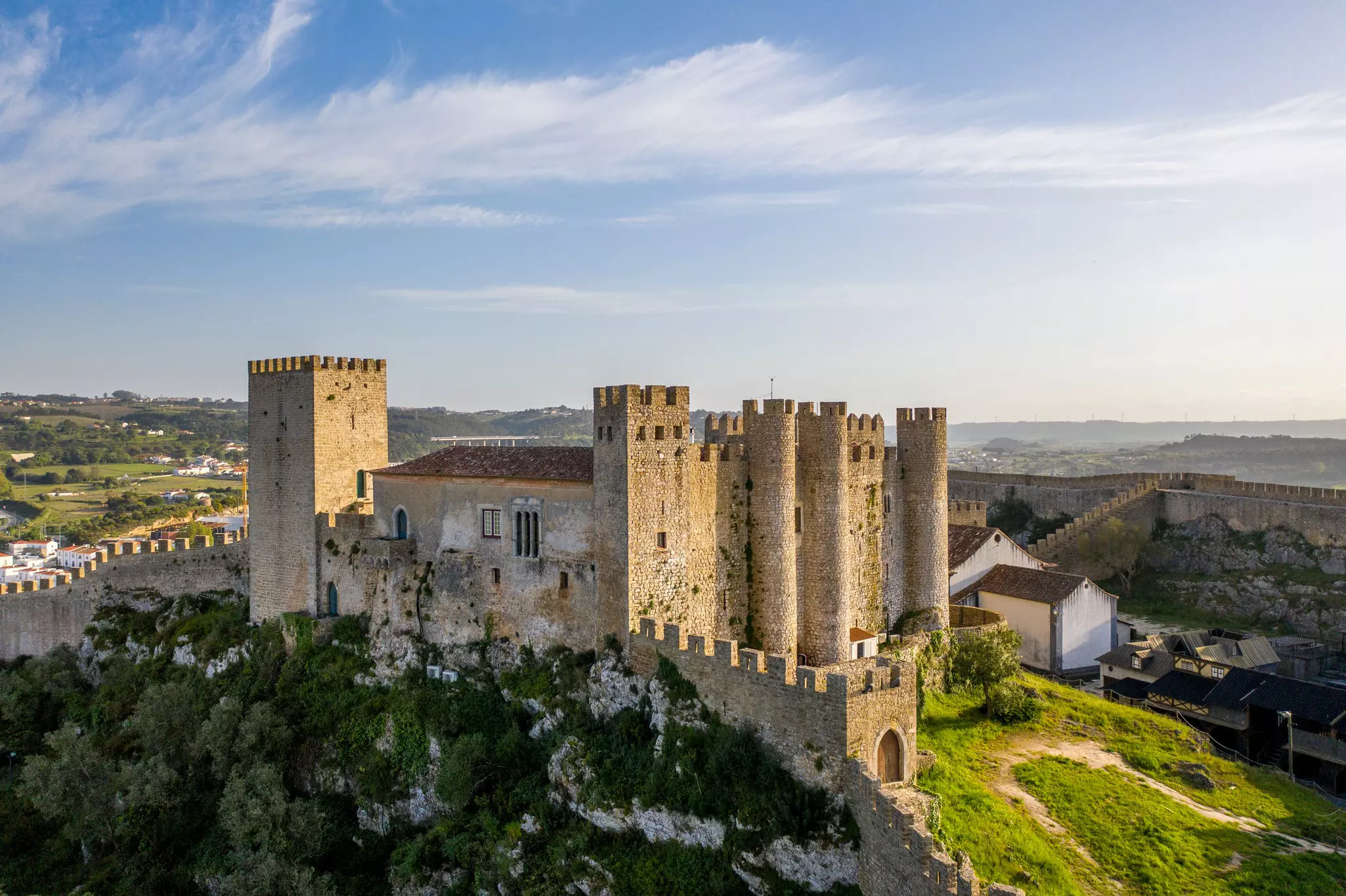 A medieval stone castle with many towers on top of a hillside; walls extend from the castle on two sides into the distance.