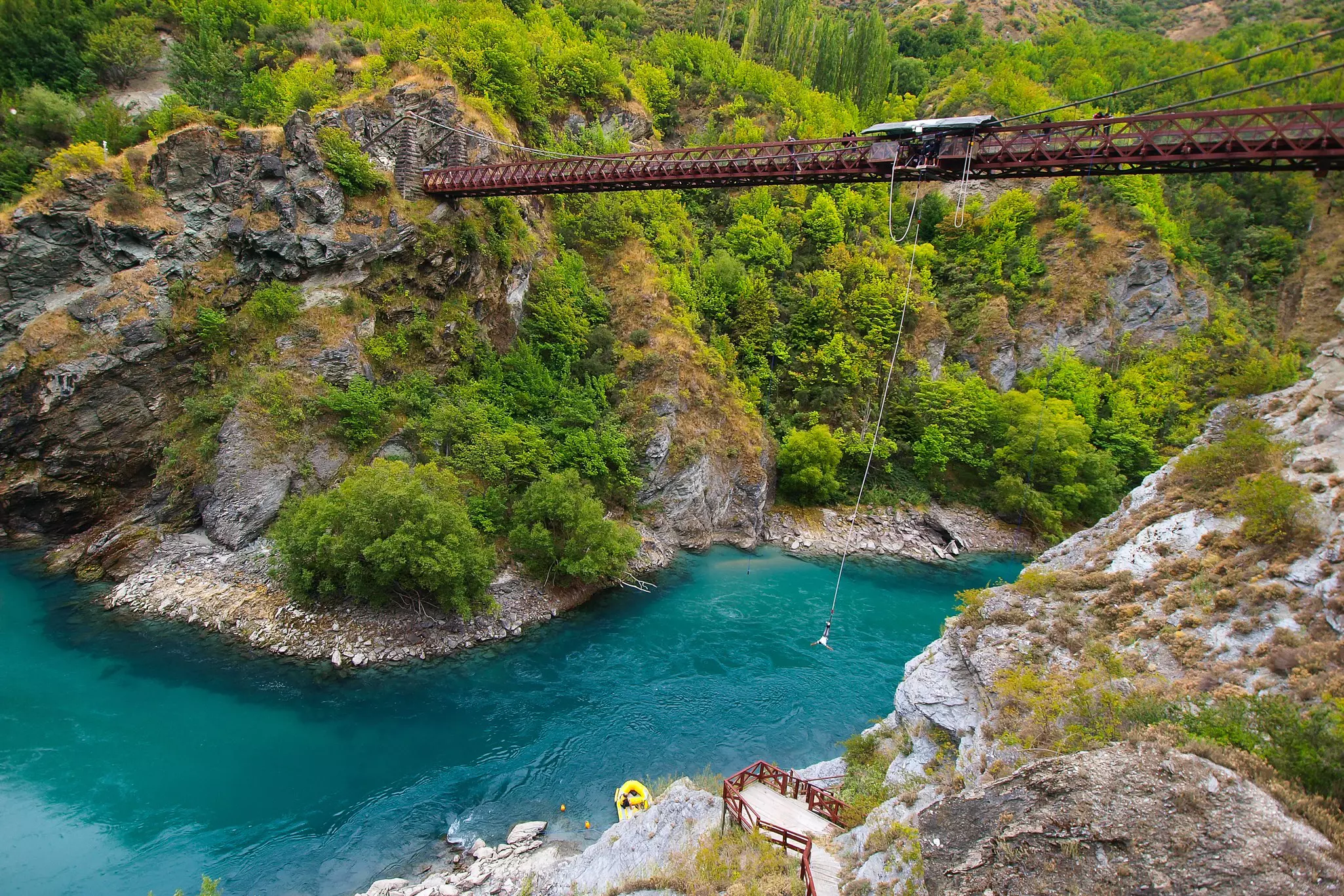 A bridge over a gorge with a fast-flowing river. A person hangs suspended from a rope having done a bungy jump off the bridge