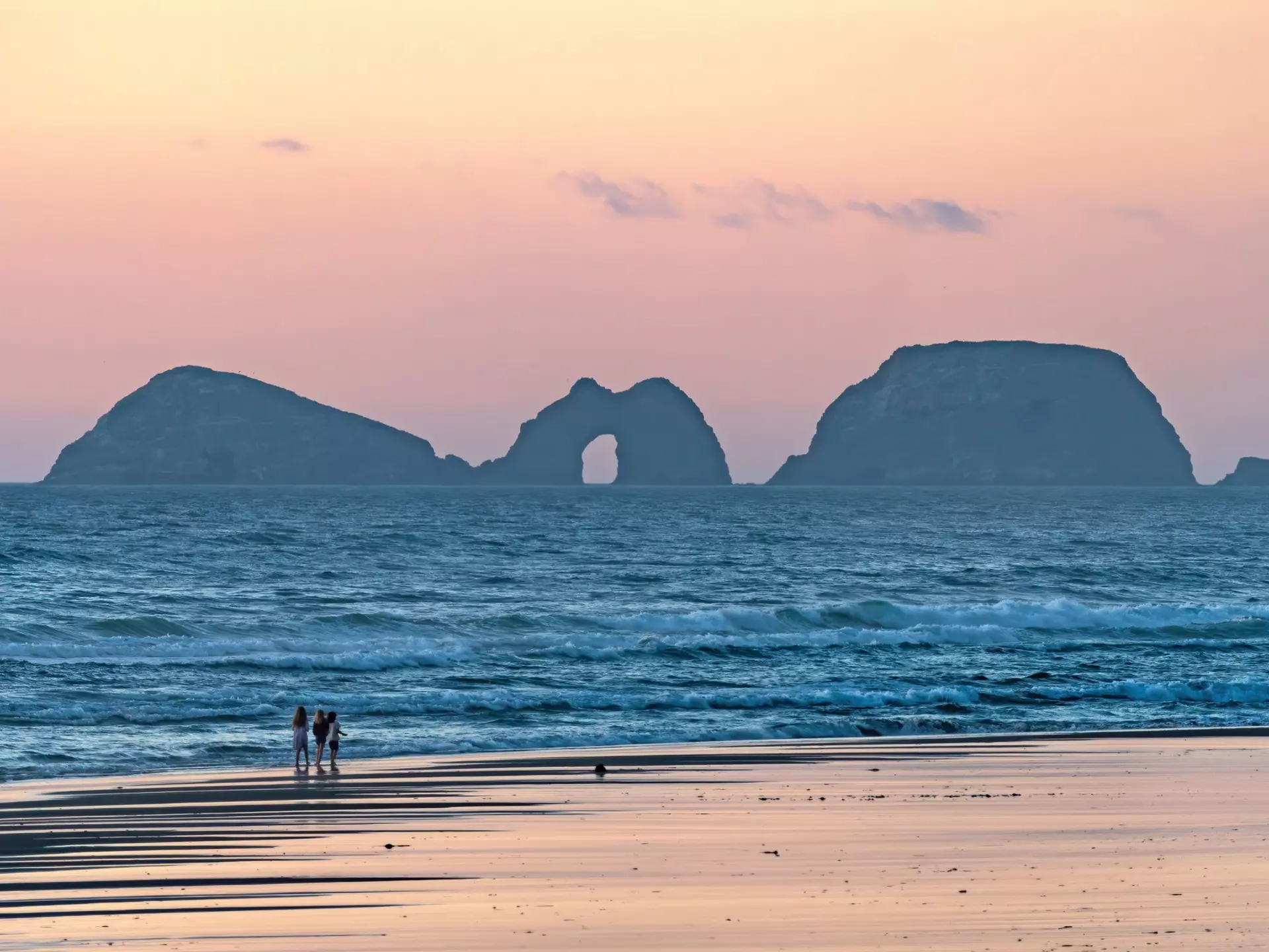 A group of people walk along the ocean coast at Cape Lookout State Park in Oregon at twilight.