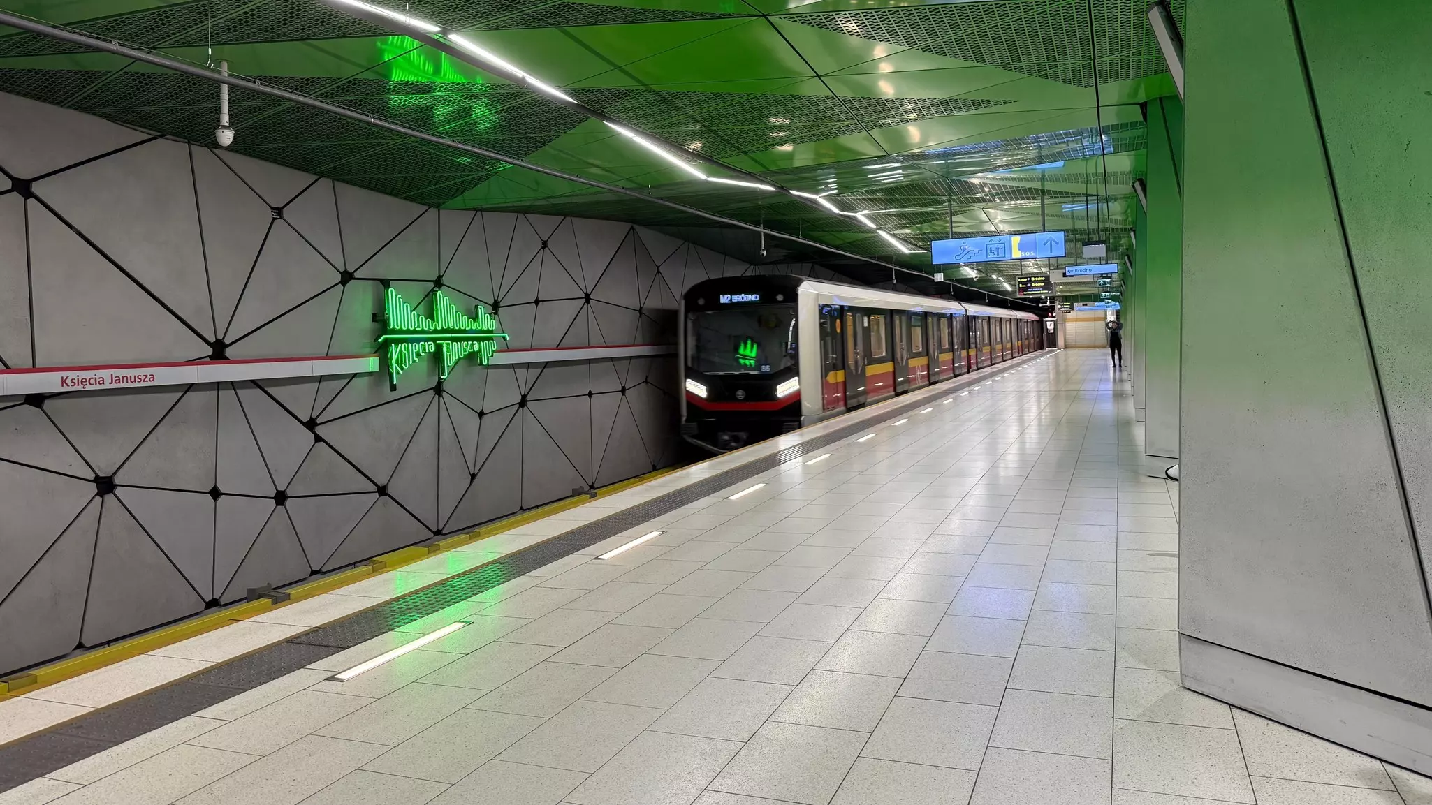 A sleek subway train with yellow, black and red doors at a platform in a station with green walls and ceiling