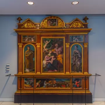 A gilded Renaissance altarpiece of the Virgin and saints on a pale blue wall.