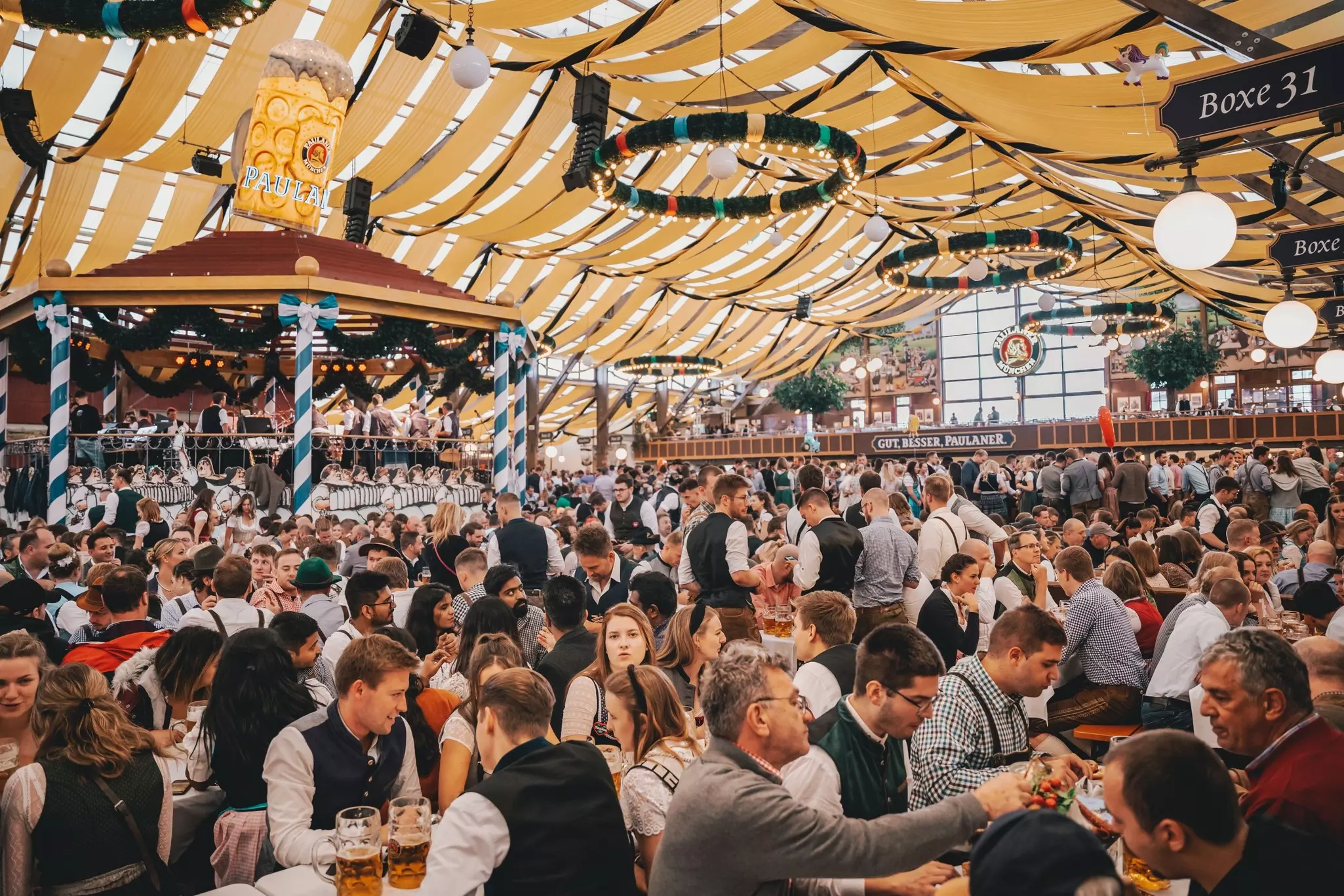 People sitting in beer tent at Oktoberfest Munich  Celebrating cheerful people drinking beer at world famous folk festival, dancing to bavarian music.