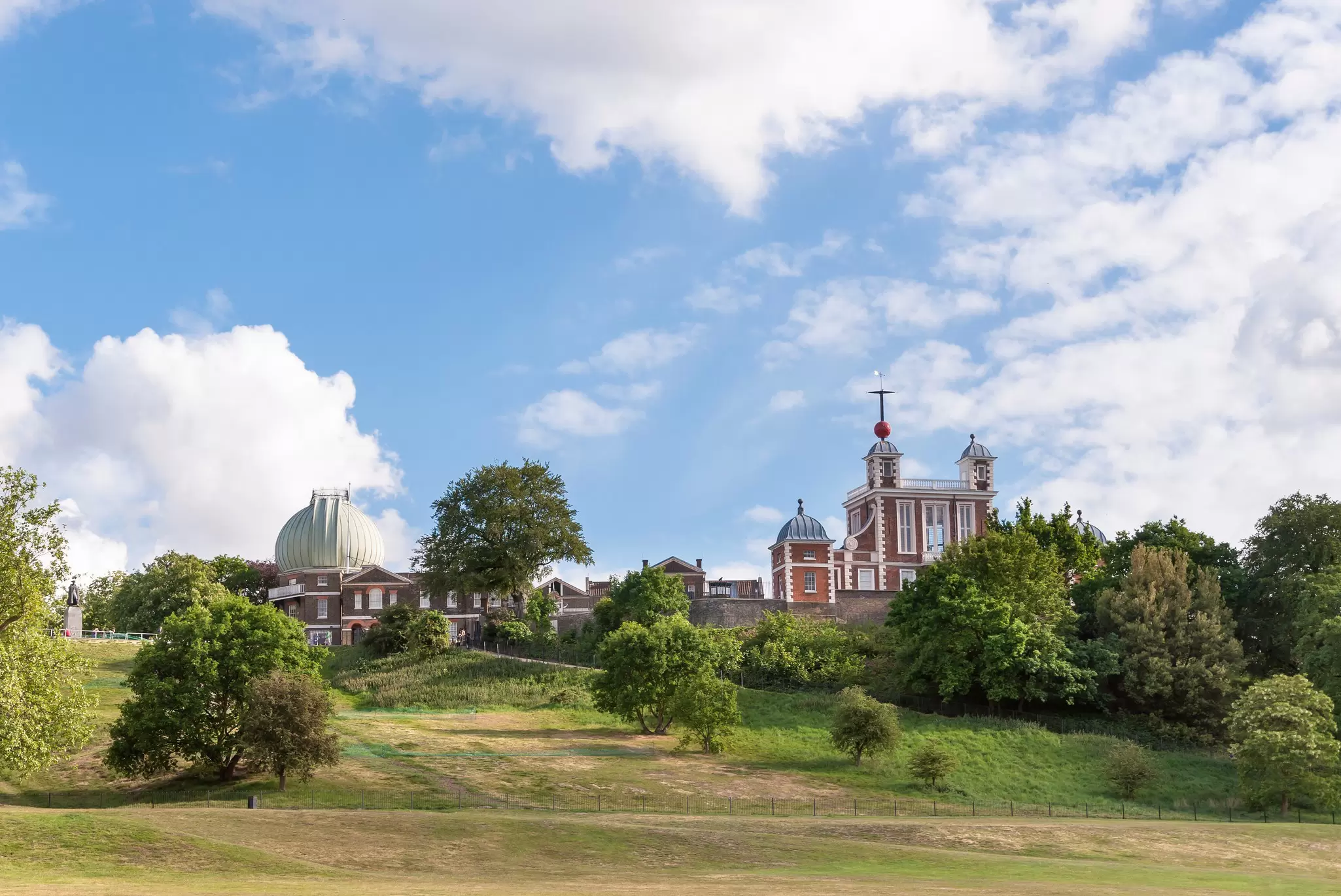 A large expanse of green with a red-brick observatory building at the top of a hill