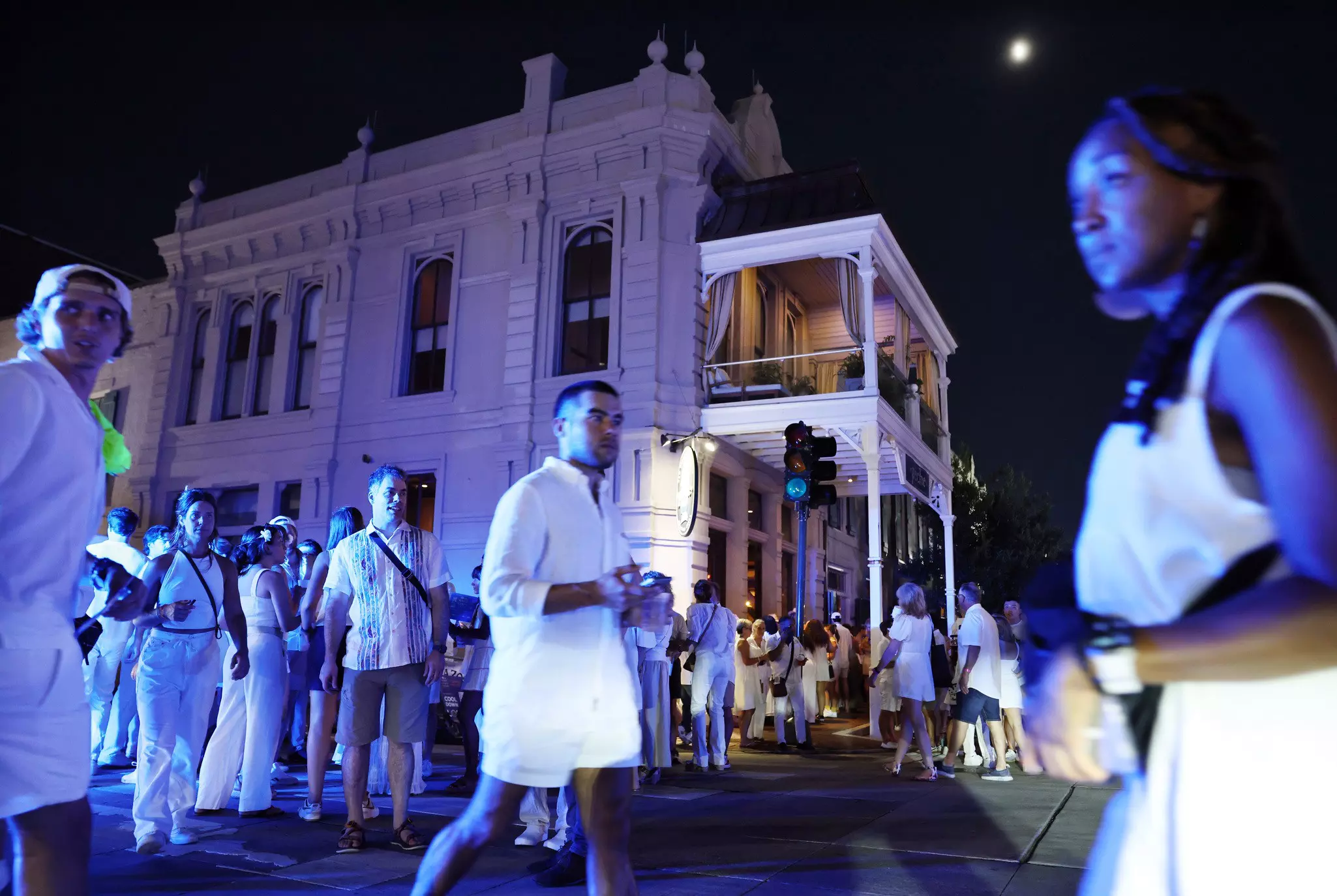 People in white outfits walk in front of a historic mansion in New Orleans