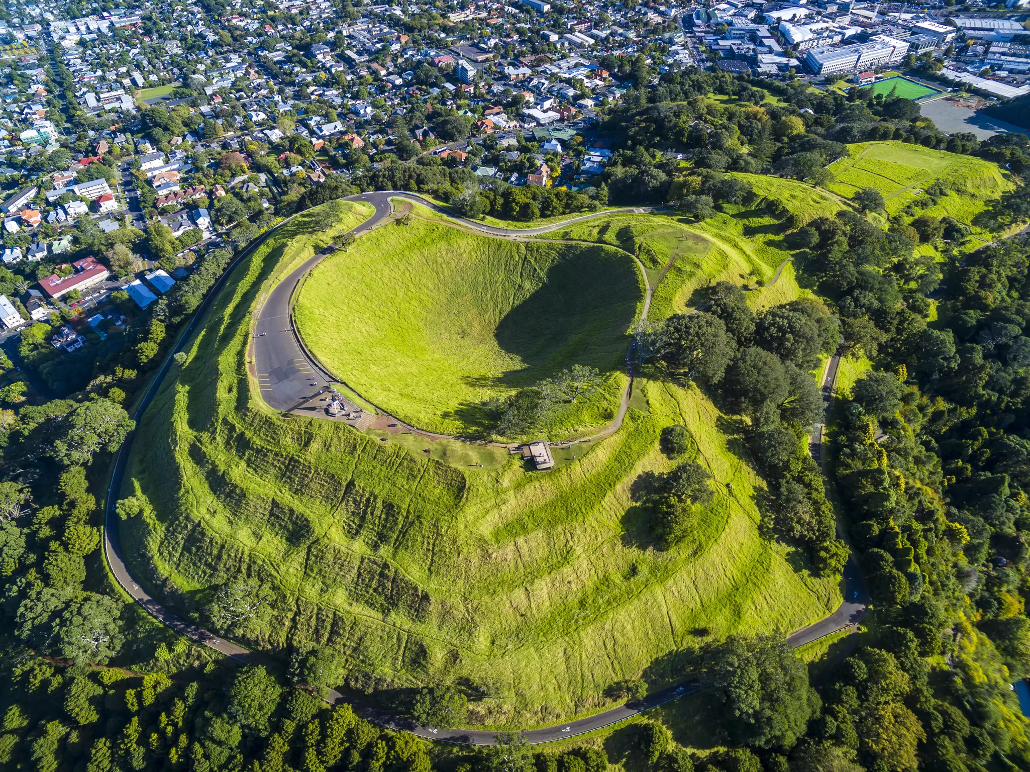 An aerial view of a green terraced hill with a pathway around the top perimeter.