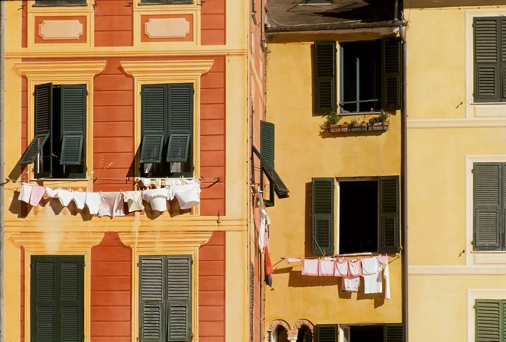 Facades of yellow and orange buildings with green shutters and laundry hanging from the windows