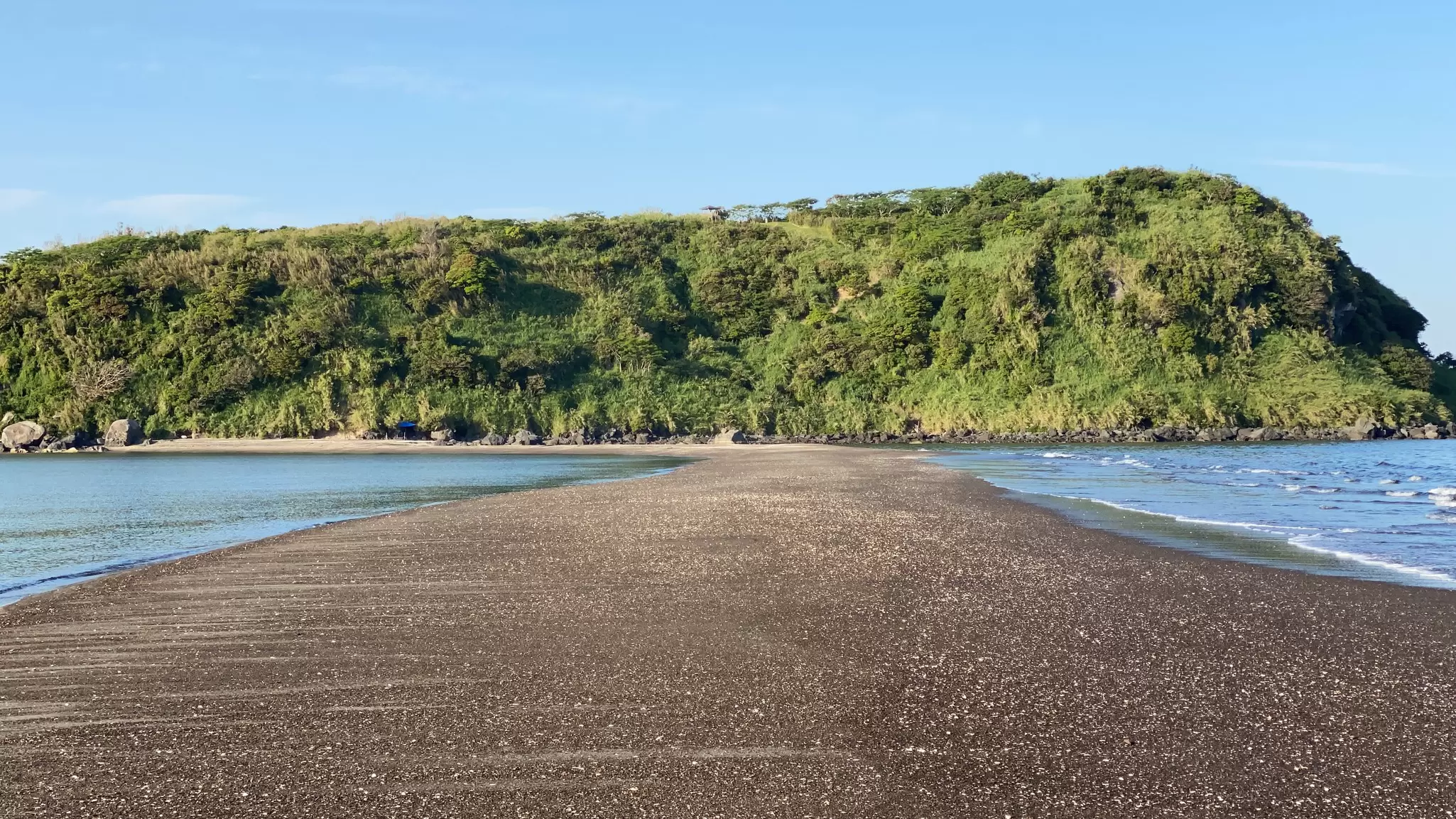 A sandbar between water leads to a forested small island.
