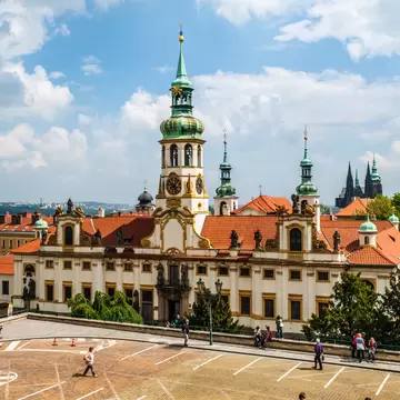Exterior of Loreto/Loreta in Prague, Czech Republic.  Pedestrians walking and blue sky.