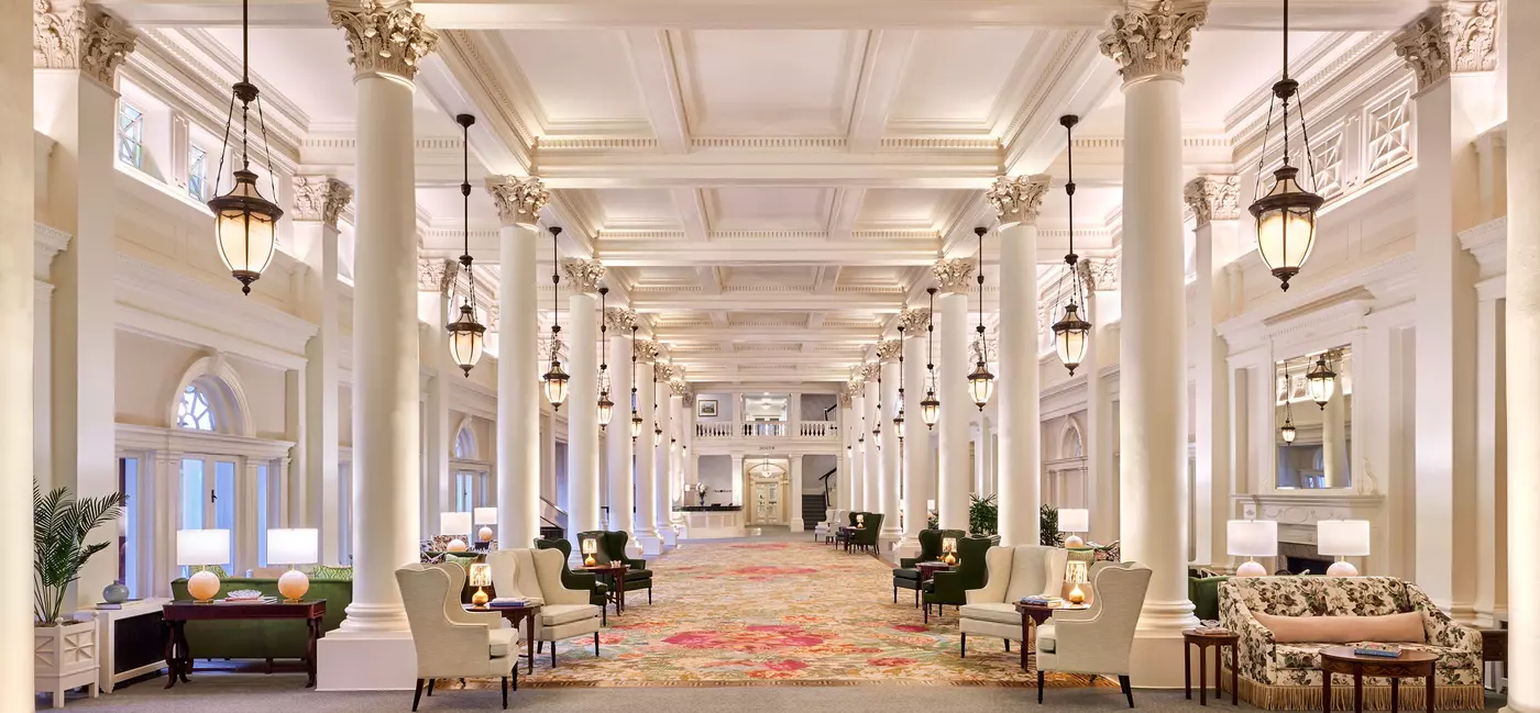 A great hall lined with white columns, lanterns hanging from the ceiling, and plush seating