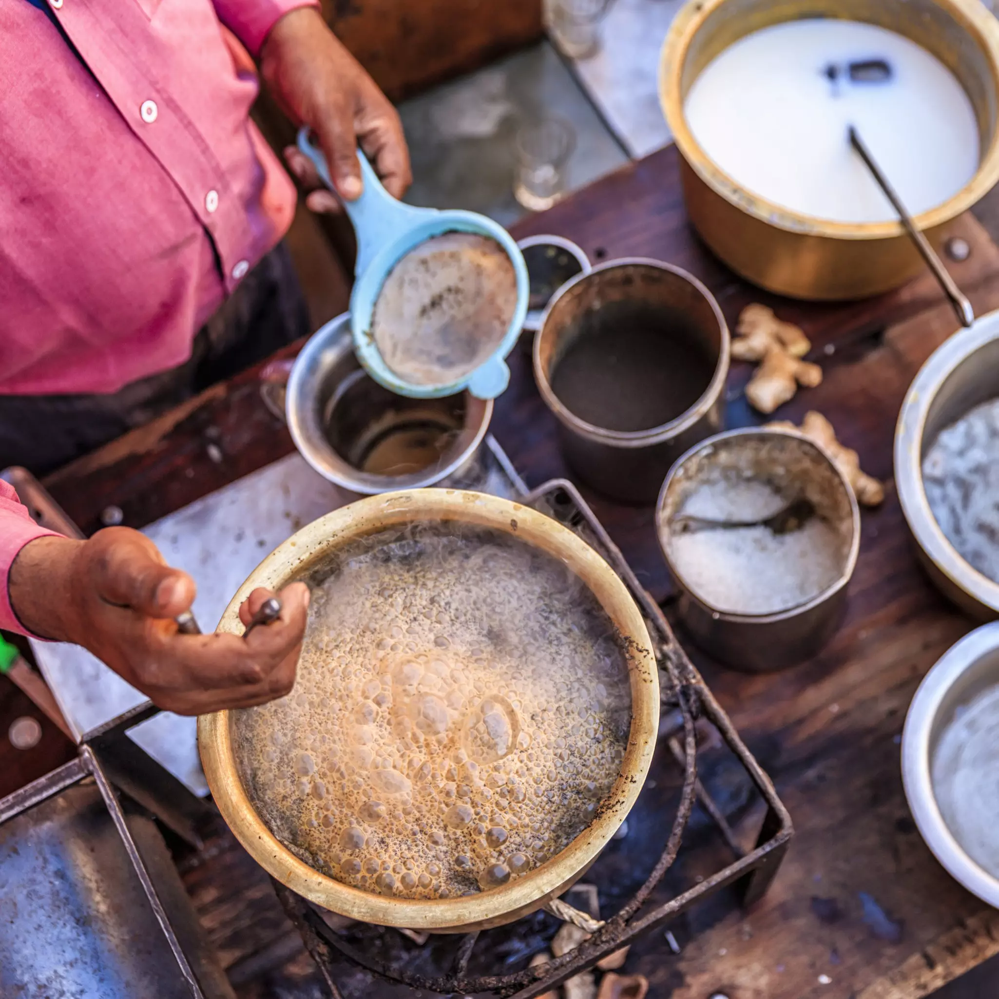A man prepares masala chai over a bubbling pot at a street stall.