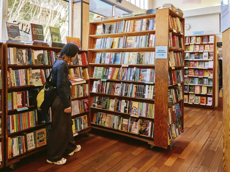 A woman in dark clothes with a yellow and black bag admires a stand of books in a bookstore.