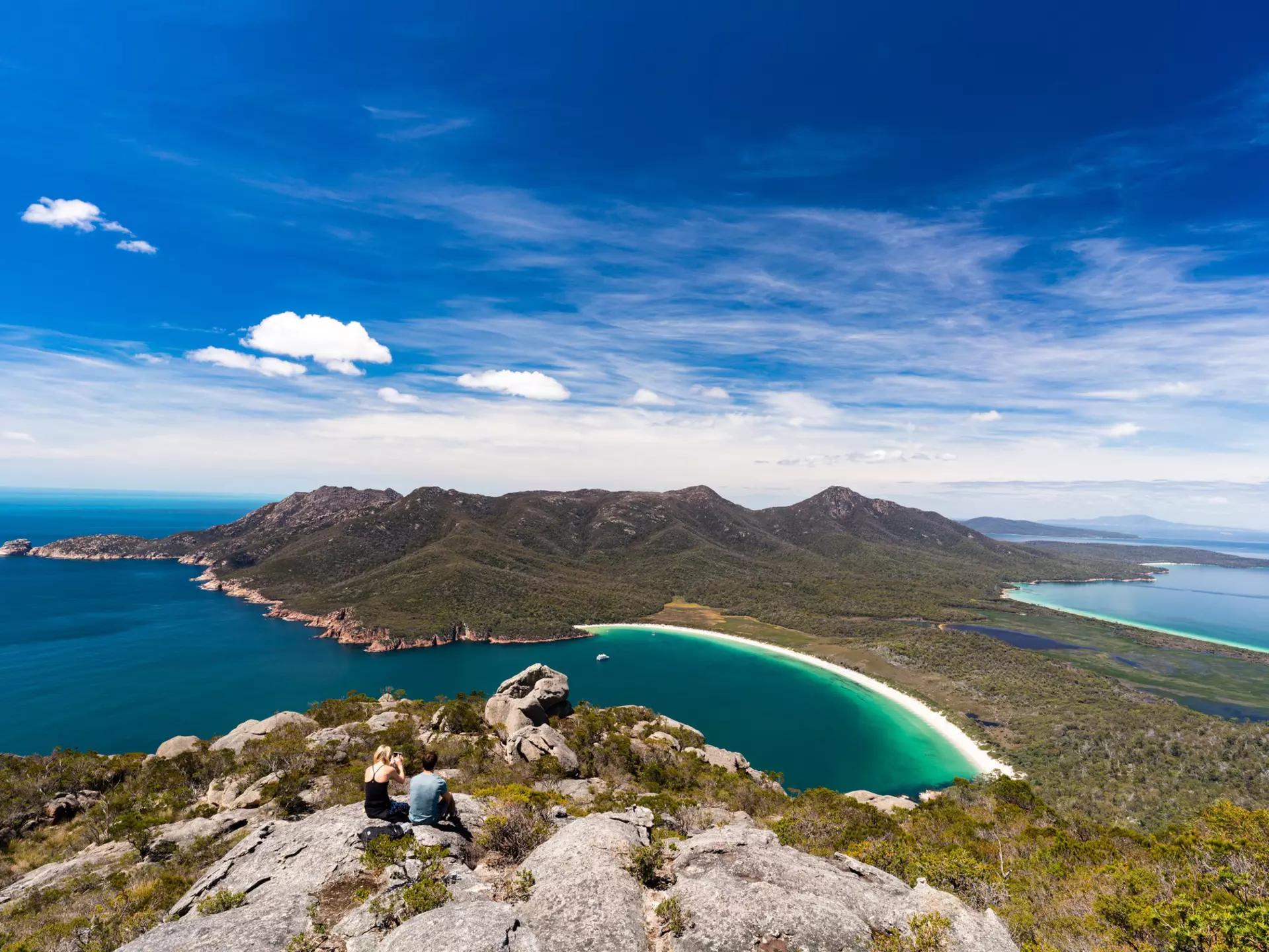 An aerial view of two people on top of Mt Amos overlooking Wineglass Bay in Tasmania
