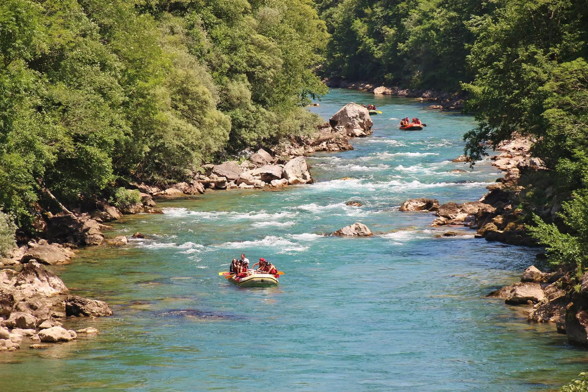 People in rafts paddling down a river in Montenegro with areas of rapids.