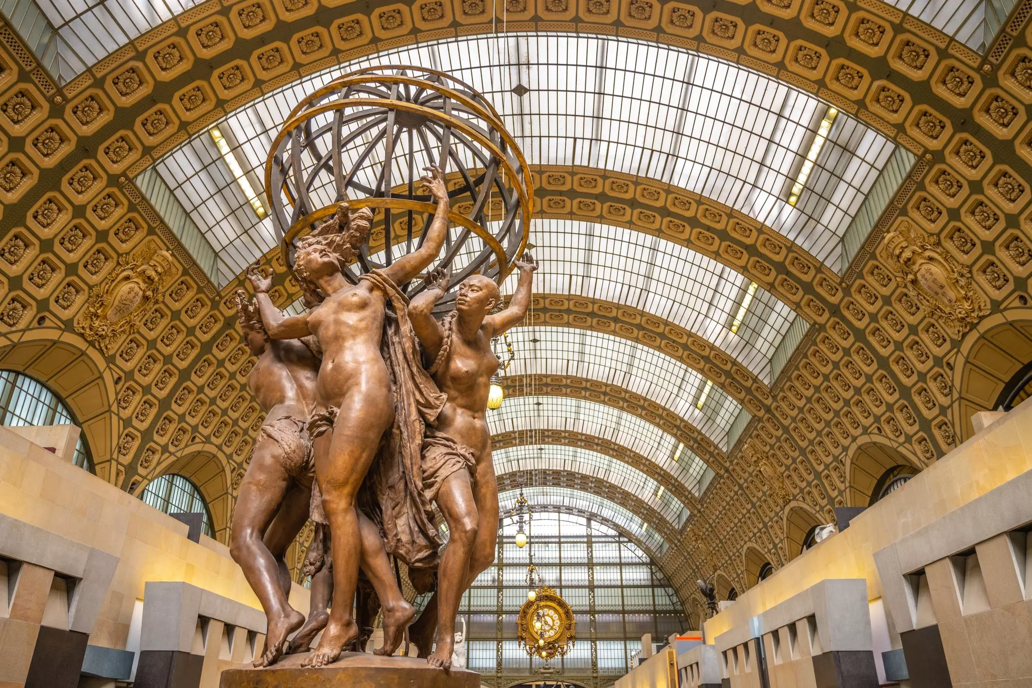 A sculpture of four figures holding a globe aloft in the center of a display space with a vaulted ceiling