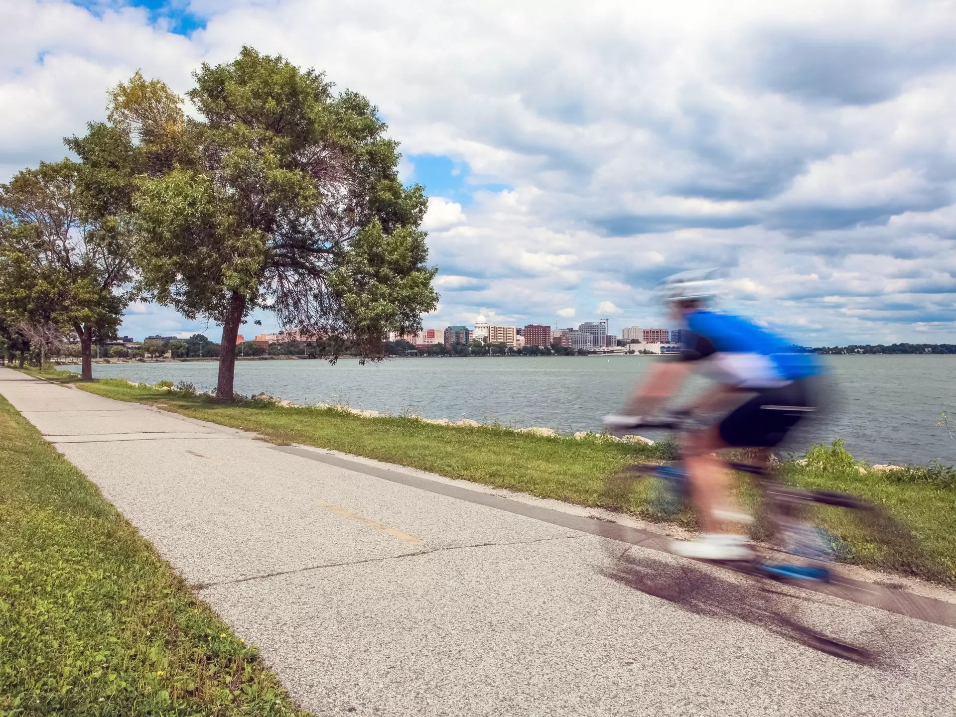 Motion blur of a person riding a bicycle on a lakeside bike path in Madison, Wisconsin with green trees and grass