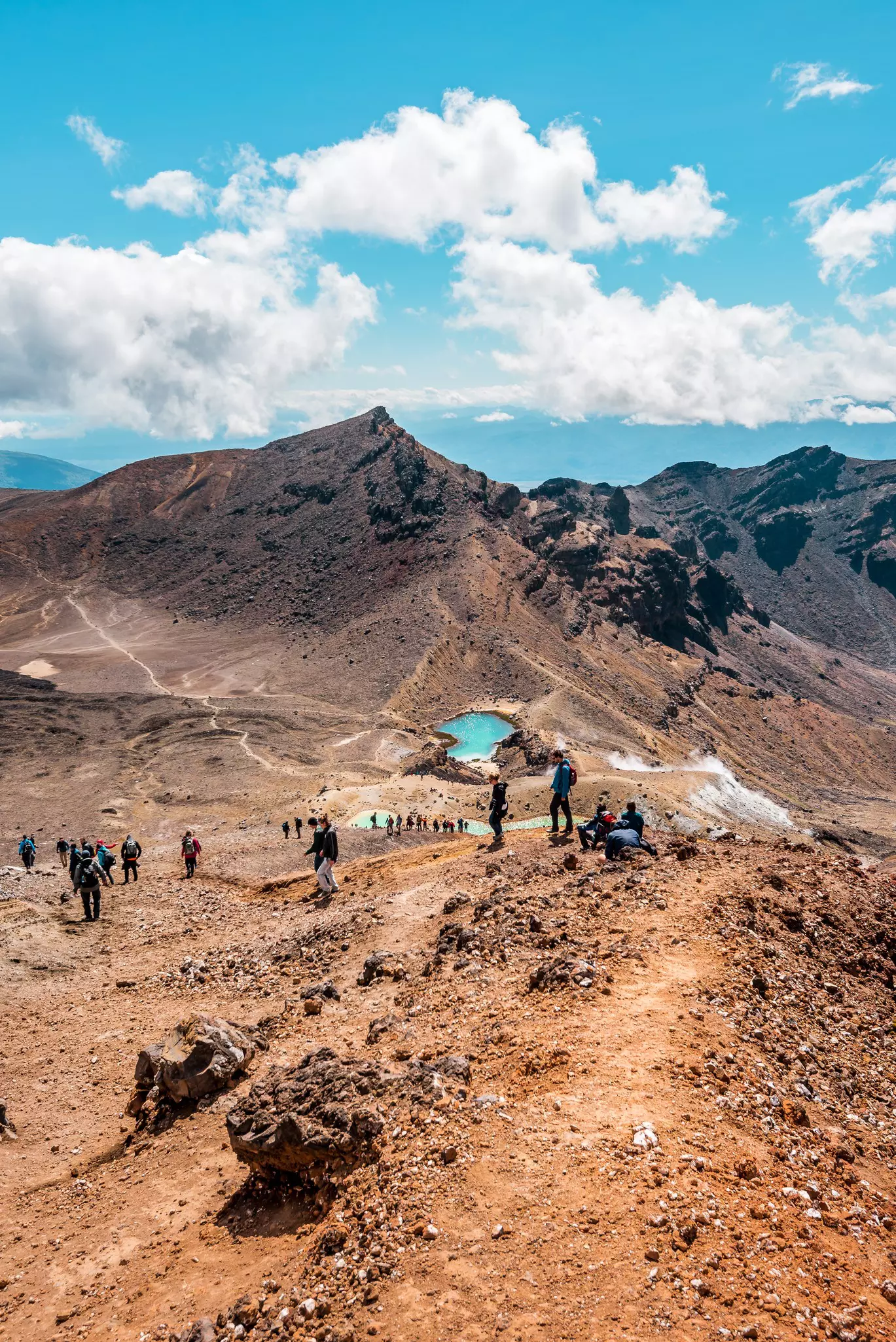 Three green lakes viewed from above with hikers following a rocky trail down towards them