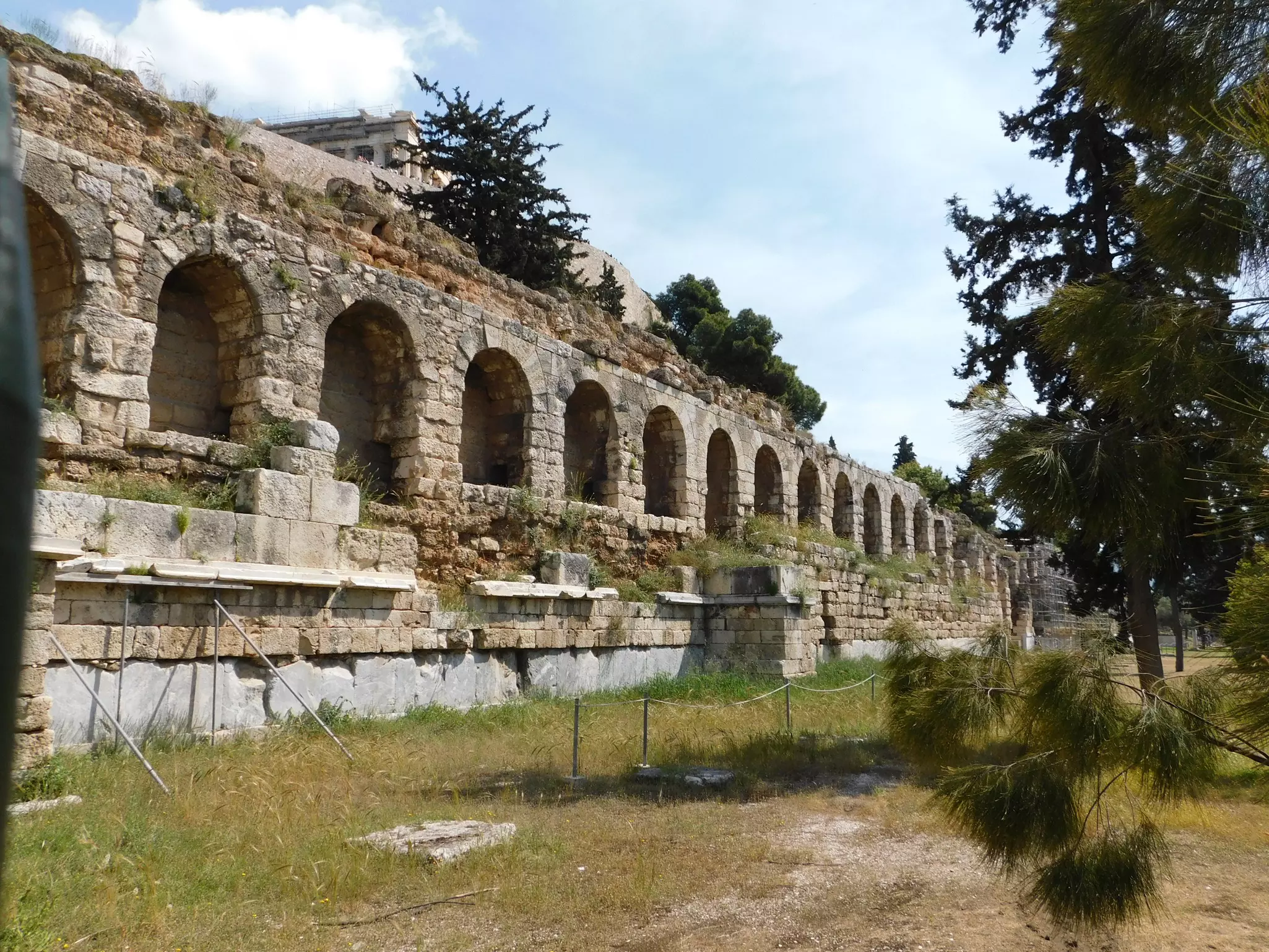 Stone ruins with curved archways in a grassy field on a sunny day.