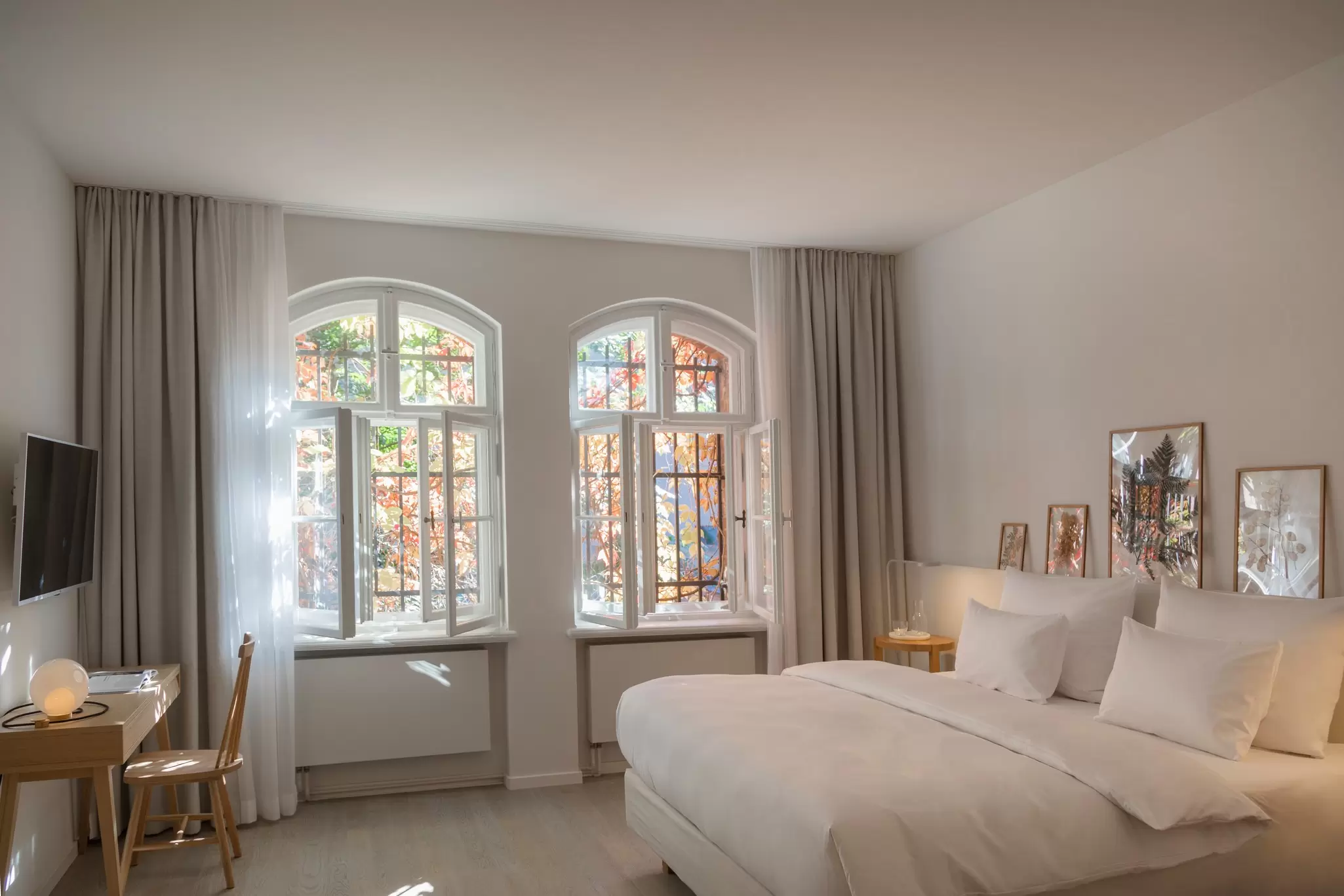 A stylish spacious hotel room with white and beige furnishings bathed in light through large windows; Wilmina, Berlin