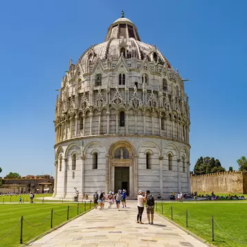 Visitors on a path leading to the domed marble Baptistery on the Piazza dei Miracoli in Pisa, with city walls at right