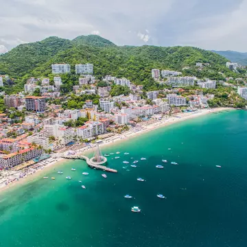 Boats dot the beachfront at Puerto Vallarta, Mexico, with hotels and green hills behind. 