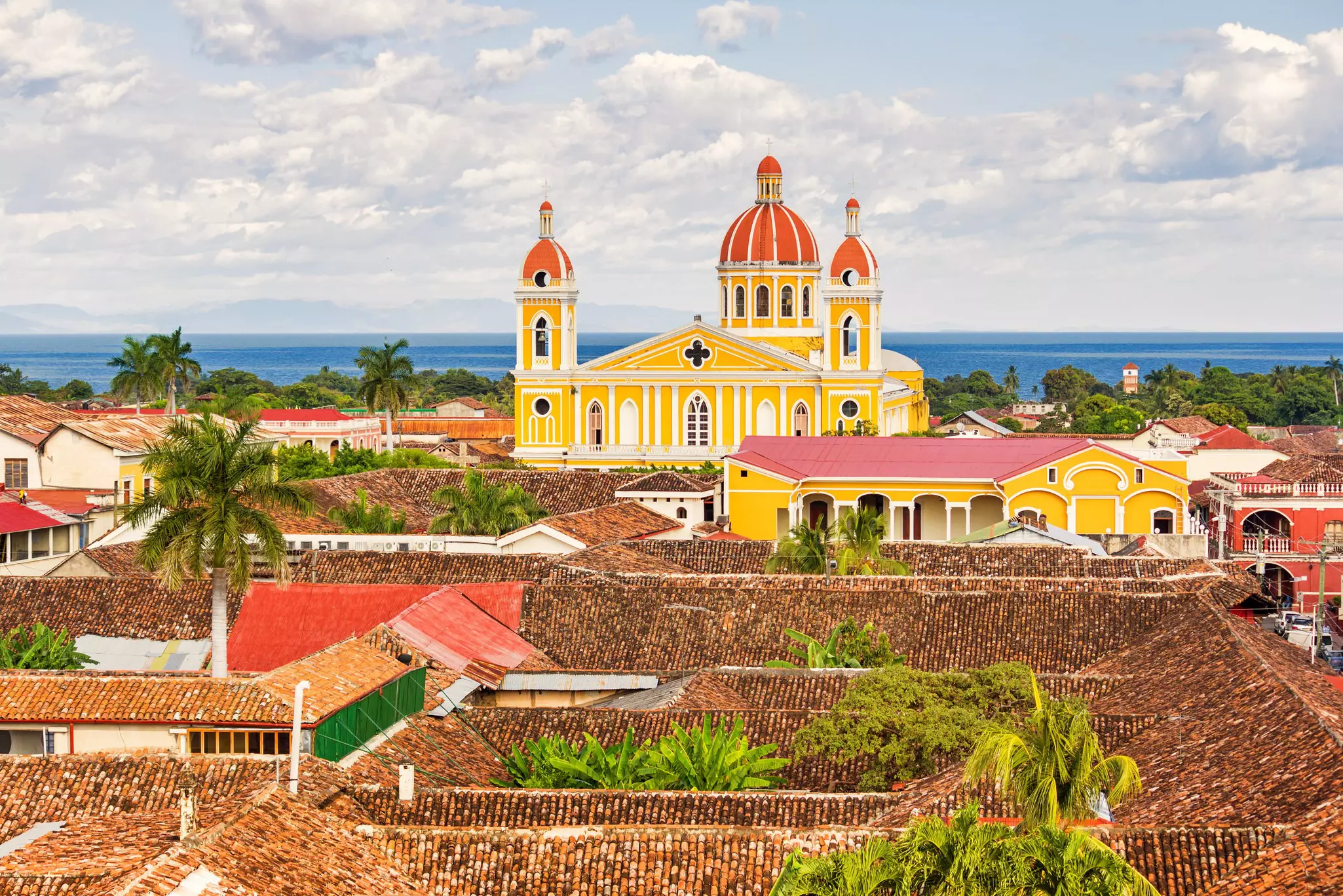 The orange, brown and red rooftops of Granada and the warm yellow Cathedral of Granada with Lake Nicaragua in the background