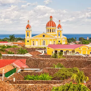 The orange, brown and red rooftops of Granada and the warm yellow Cathedral of Granada with Lake Nicaragua in the background
