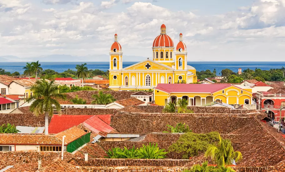 The orange, brown and red rooftops of Granada and the warm yellow Cathedral of Granada with Lake Nicaragua in the background
