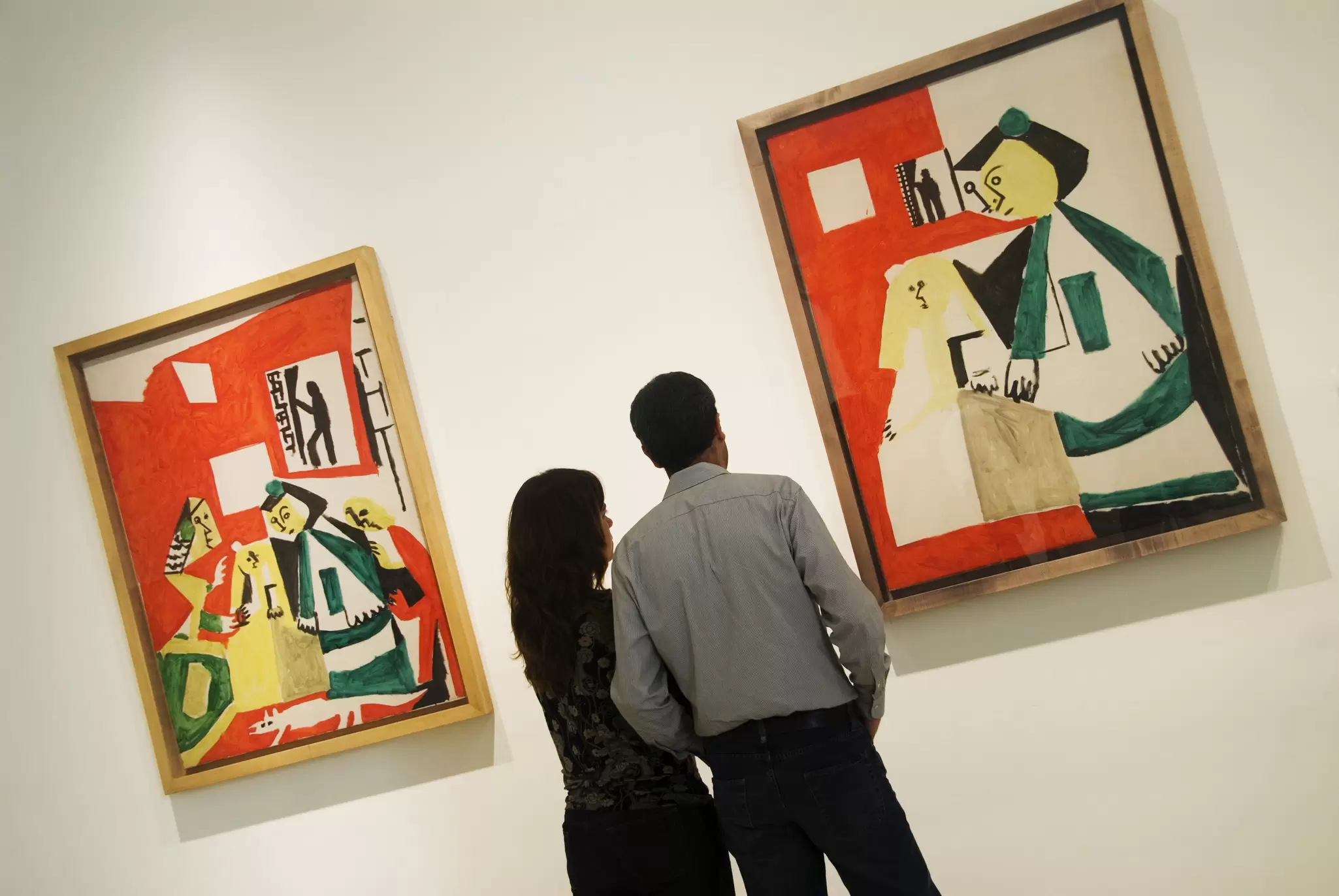 Two people stand in front of two paintings by the artist Picasso, in the Museu Picasso in Barcelona. The paintings employ Picasso's classic Cubist style.