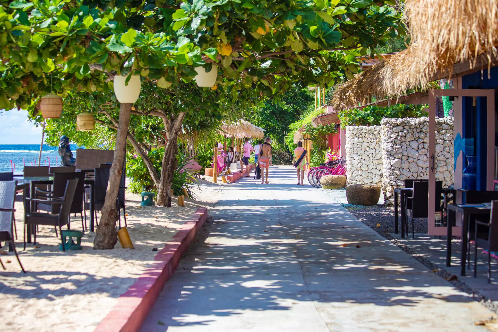 People at the end of a narrow lane between a beach and low buildings.