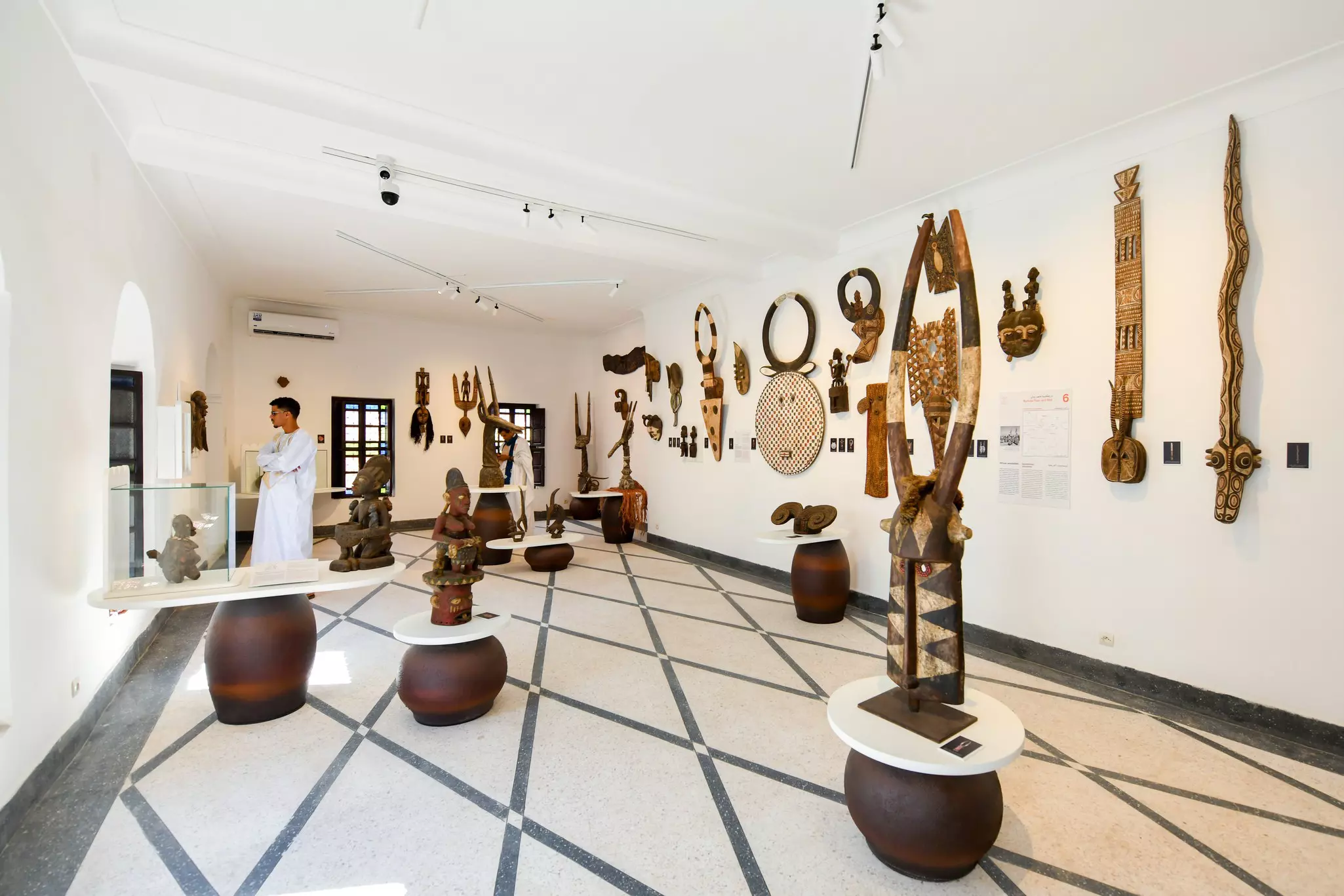A person in white clothing looks at a display on the far back wall of an exhibition gallery.