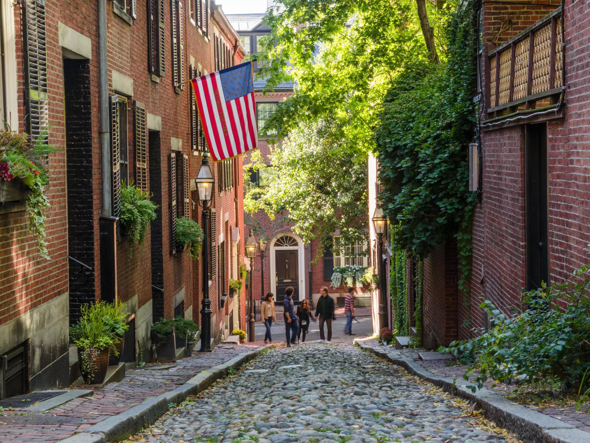 Tourists wandering along a hilly cobbled street on a sunny day.