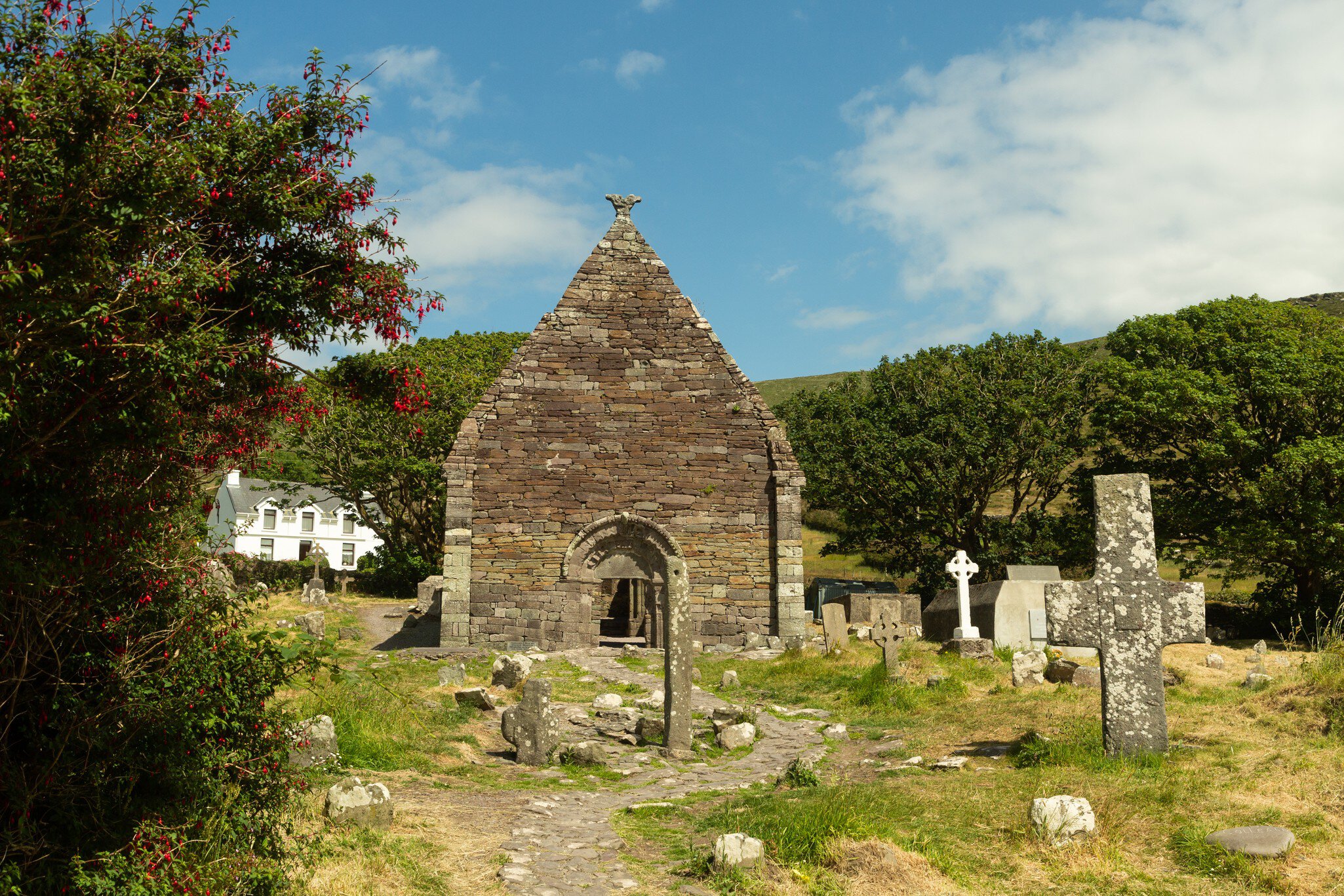12th century Kilmalkedar church and its cemetery in Count Kerry, Ireland. Blue sky and trees surrounding.