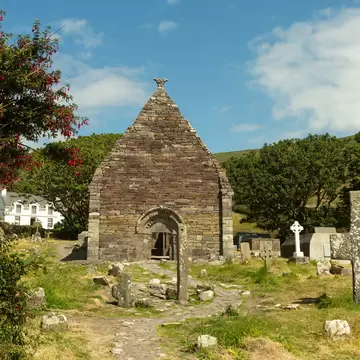 12th century Kilmalkedar church and its cemetery in Count Kerry, Ireland. Blue sky and trees surrounding.