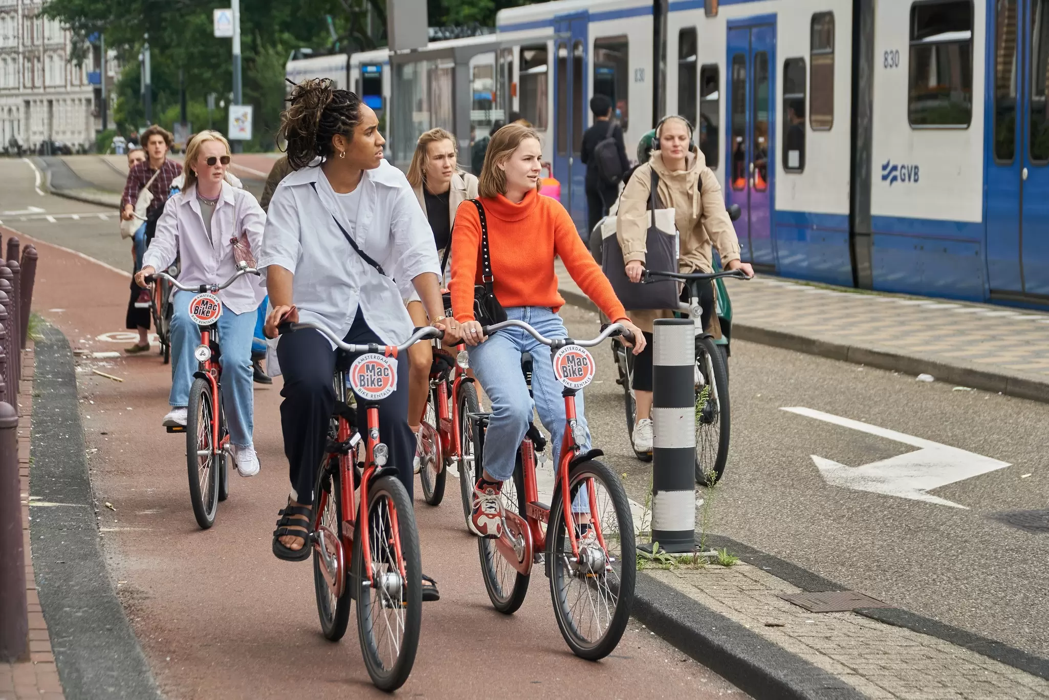 Tourists cycling on rental bikes in Amsterdam, Netherlands, with a tram in the background. 