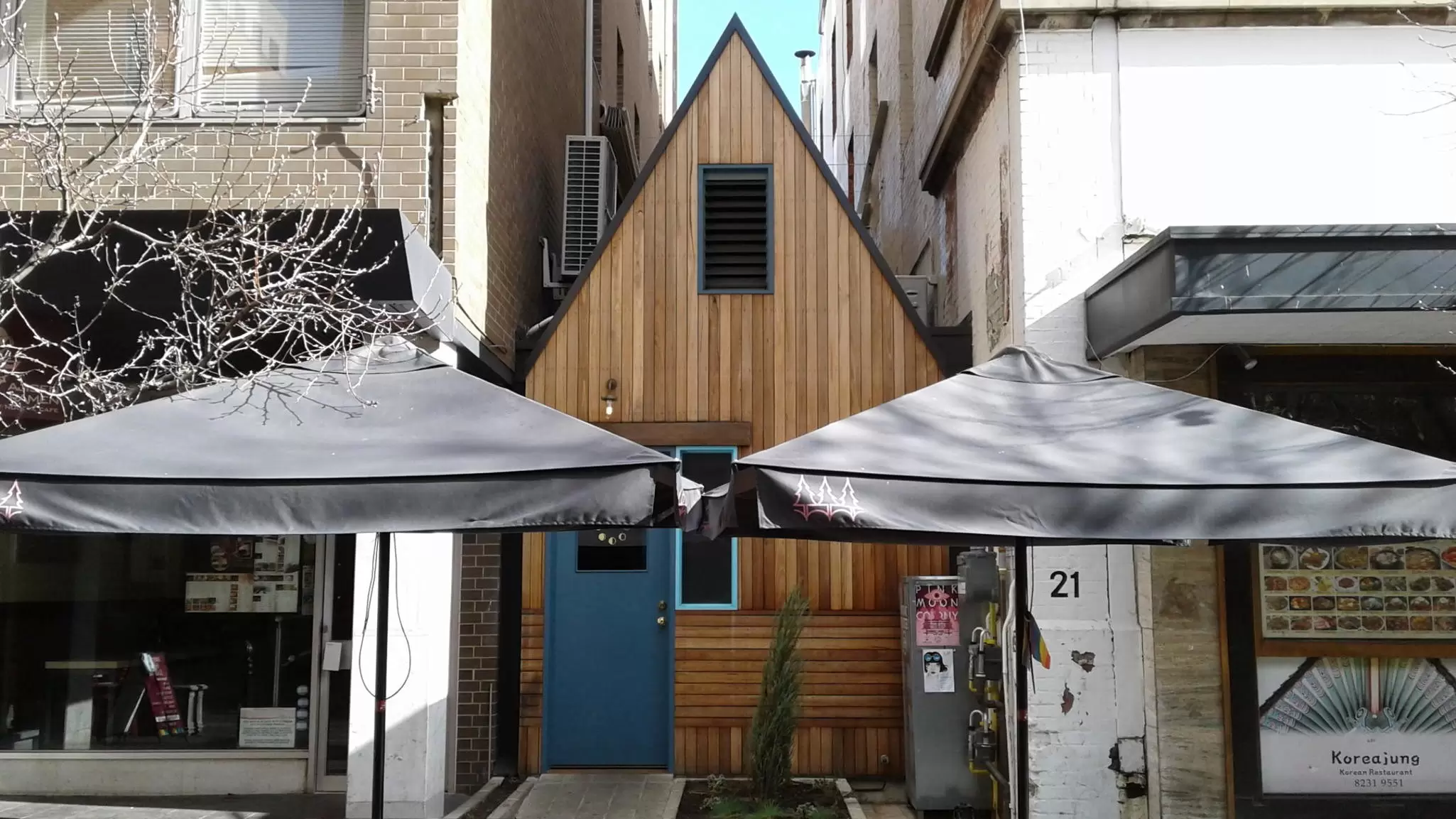 Two black sun umbrellas in front of a narrow wooden building with a steeply peaked roof.
