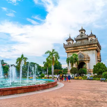 A concrete monument and archway near fountains in a garden