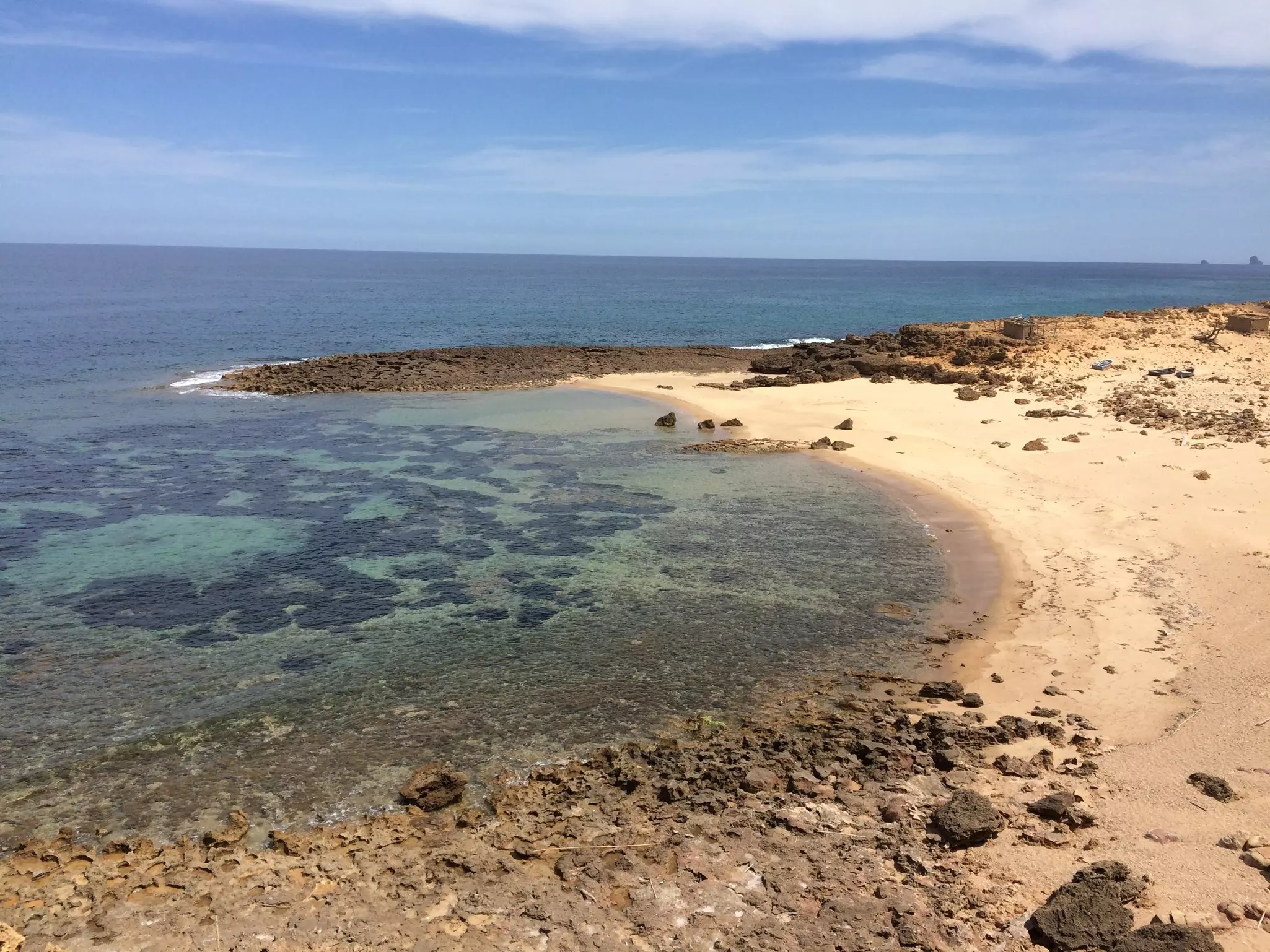 A view of an empty beach with golden sand and shallow clear water.