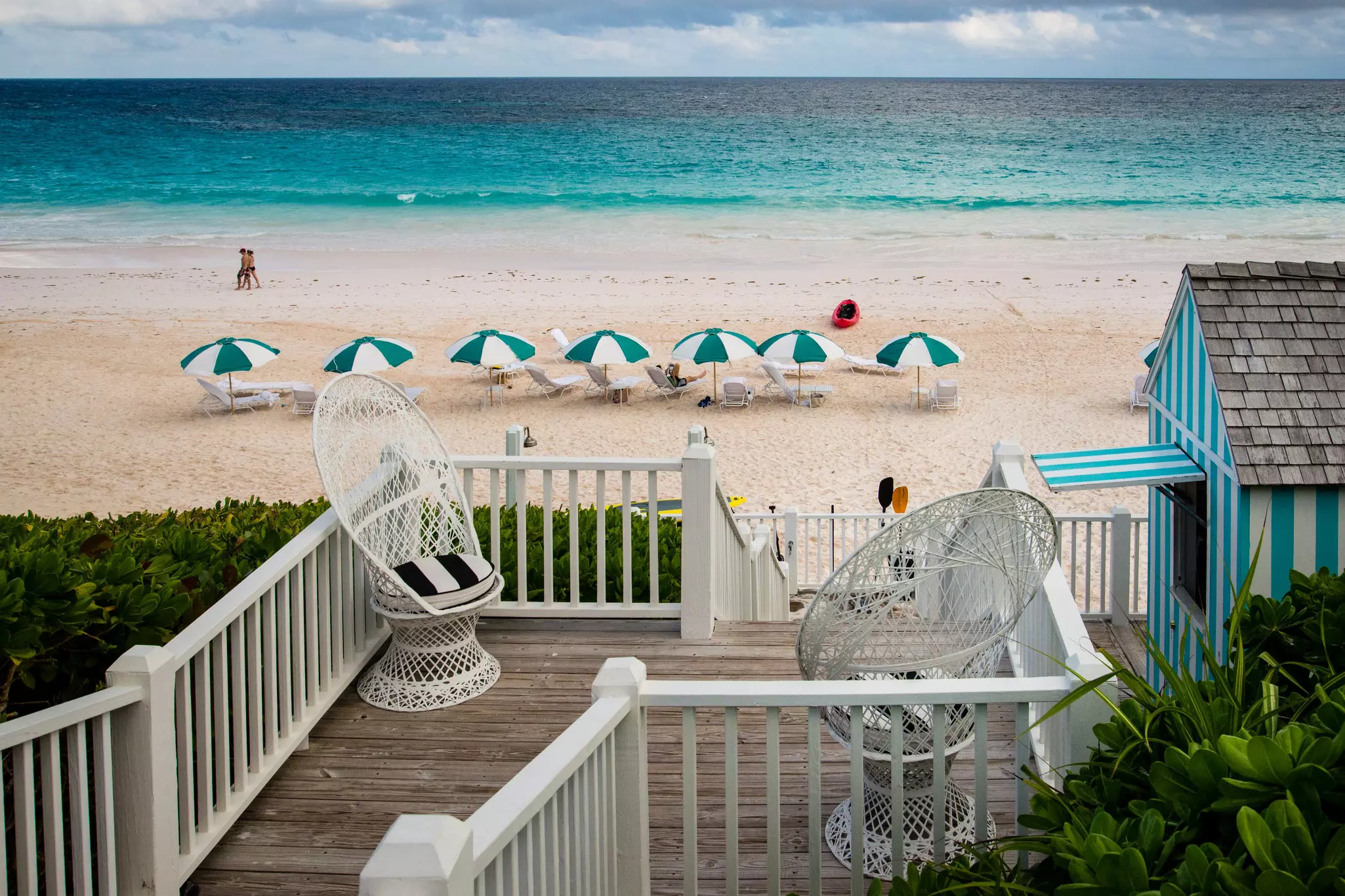 Green and white umbrellas in the sand on a beach near a shack renting paddling gear. The sky out at sea is stormy