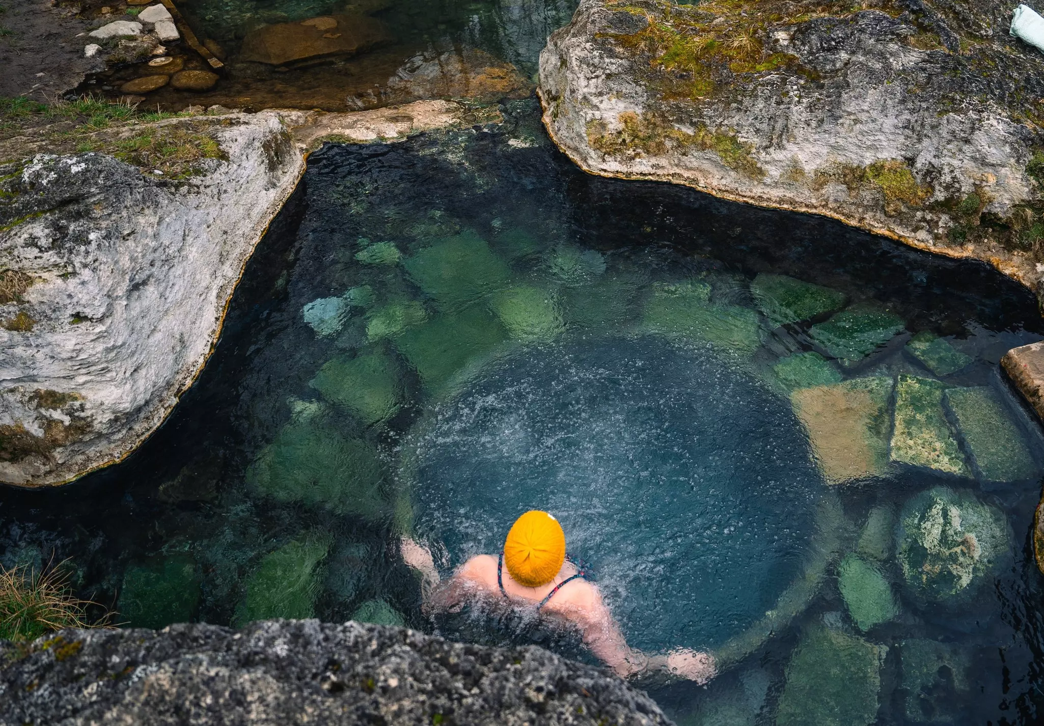 A woman in a yellow cap sits in a thermal pool in Low Tatras National Park in Slovakia.