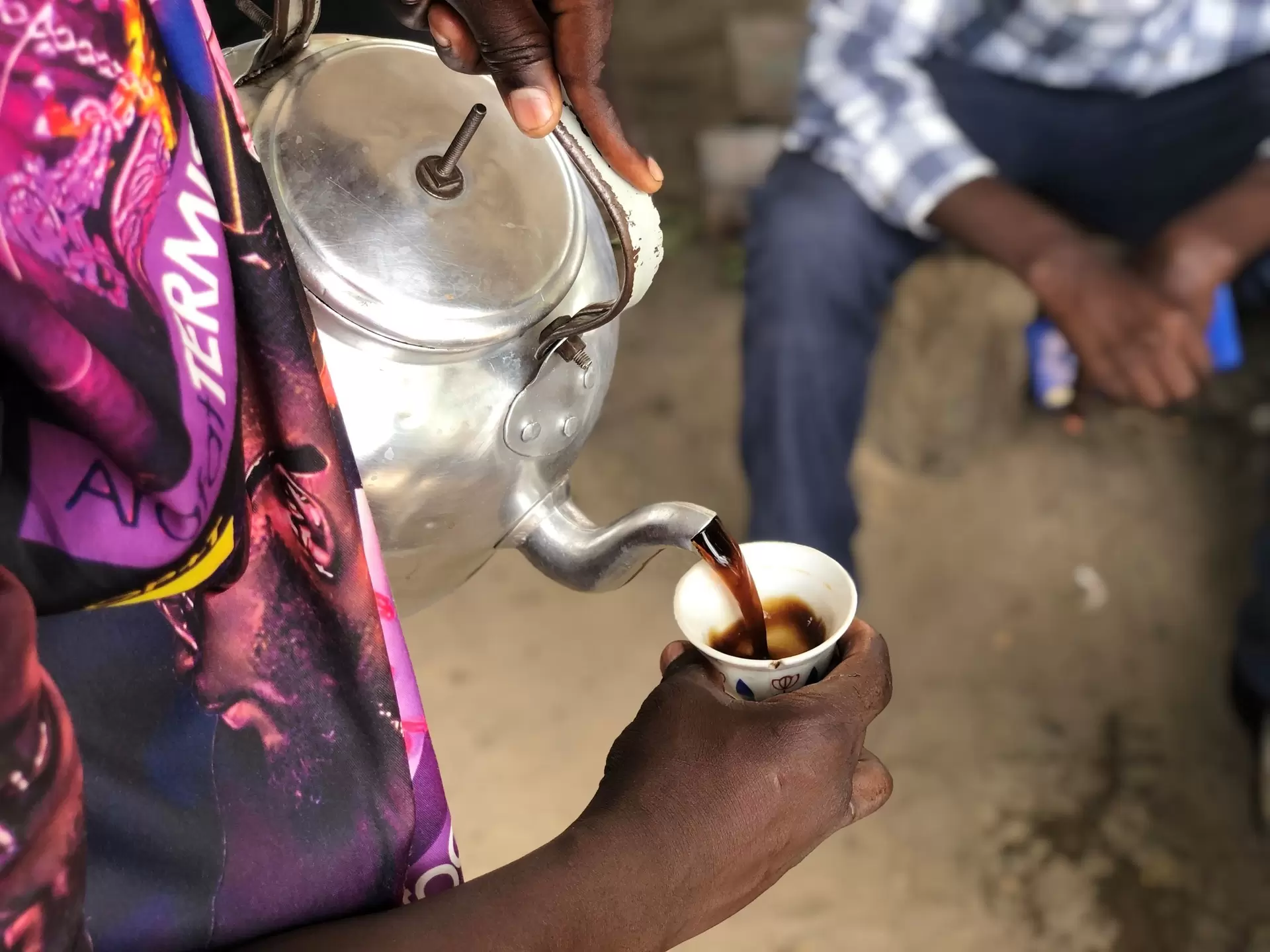 An overhead view of a person pouring coffee from a metal kettle at a street stall, Dar es Salaam, Tanzania