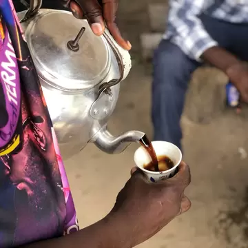 An overhead view of a person pouring coffee from a metal kettle at a street stall, Dar es Salaam, Tanzania