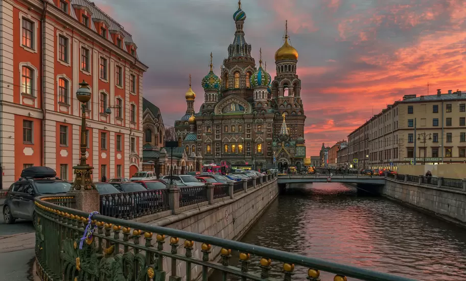 The ornate onion domes of the Church of the Savior on Spilled Blood rising over a canal in St Petersburg at a vivid sunset.