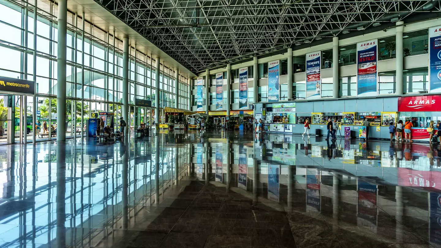 People walking through a bright, modern long-distance bus station with a wall of windows on one side
