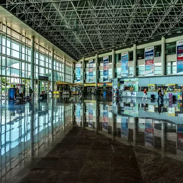 People walking through a bright, modern long-distance bus station with a wall of windows on one side
