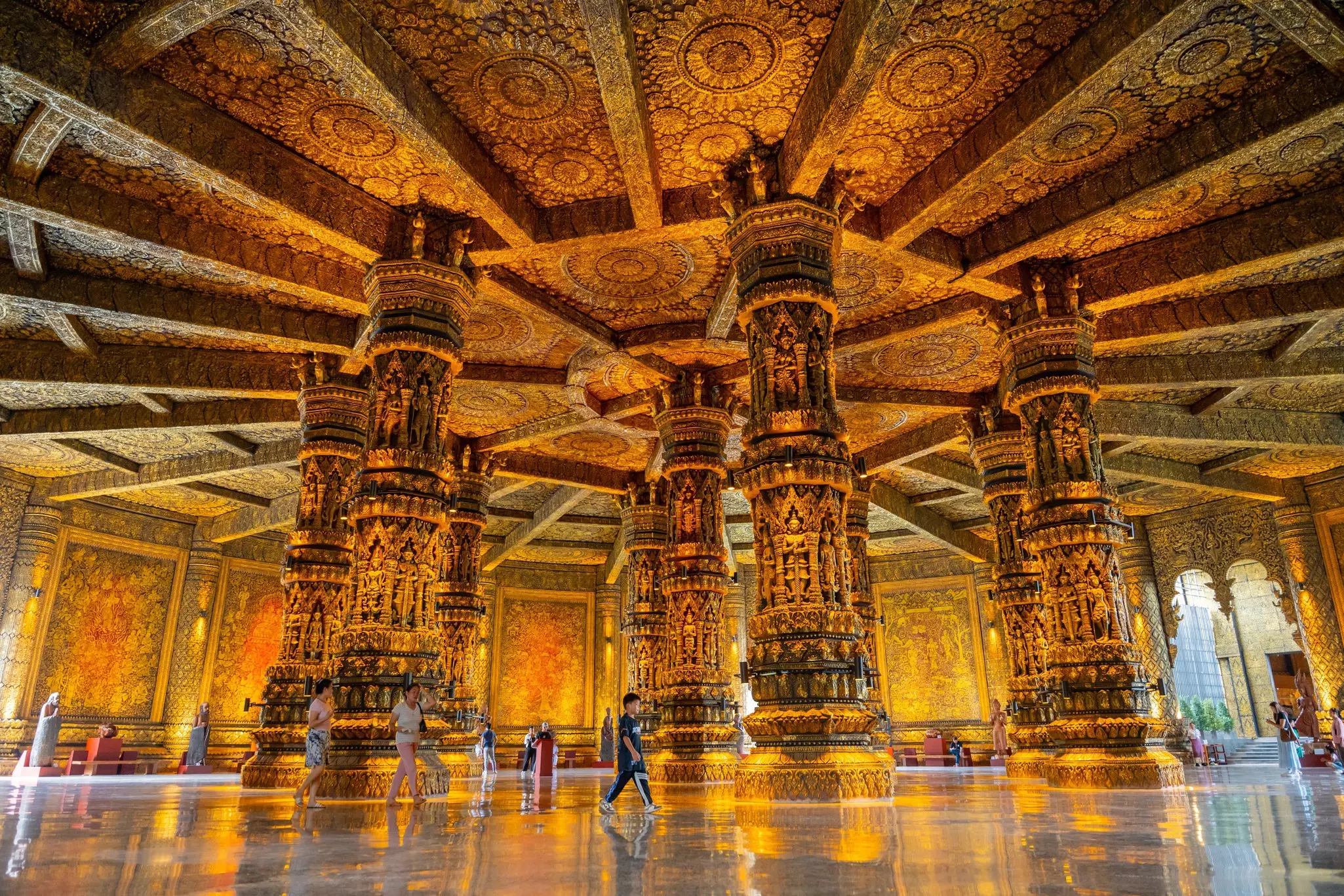 People walk through the monumental lobby of a museum with huge, carved, gilded columns.