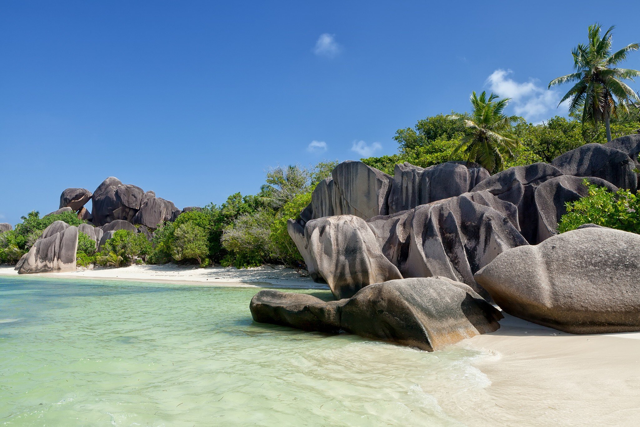 Wide shot of granite rocks with clear ocean water in the foreground.