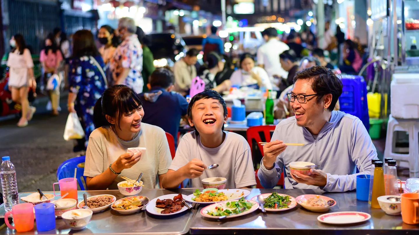 Asian family eating at a street food restaurant with crowd of people behind them
