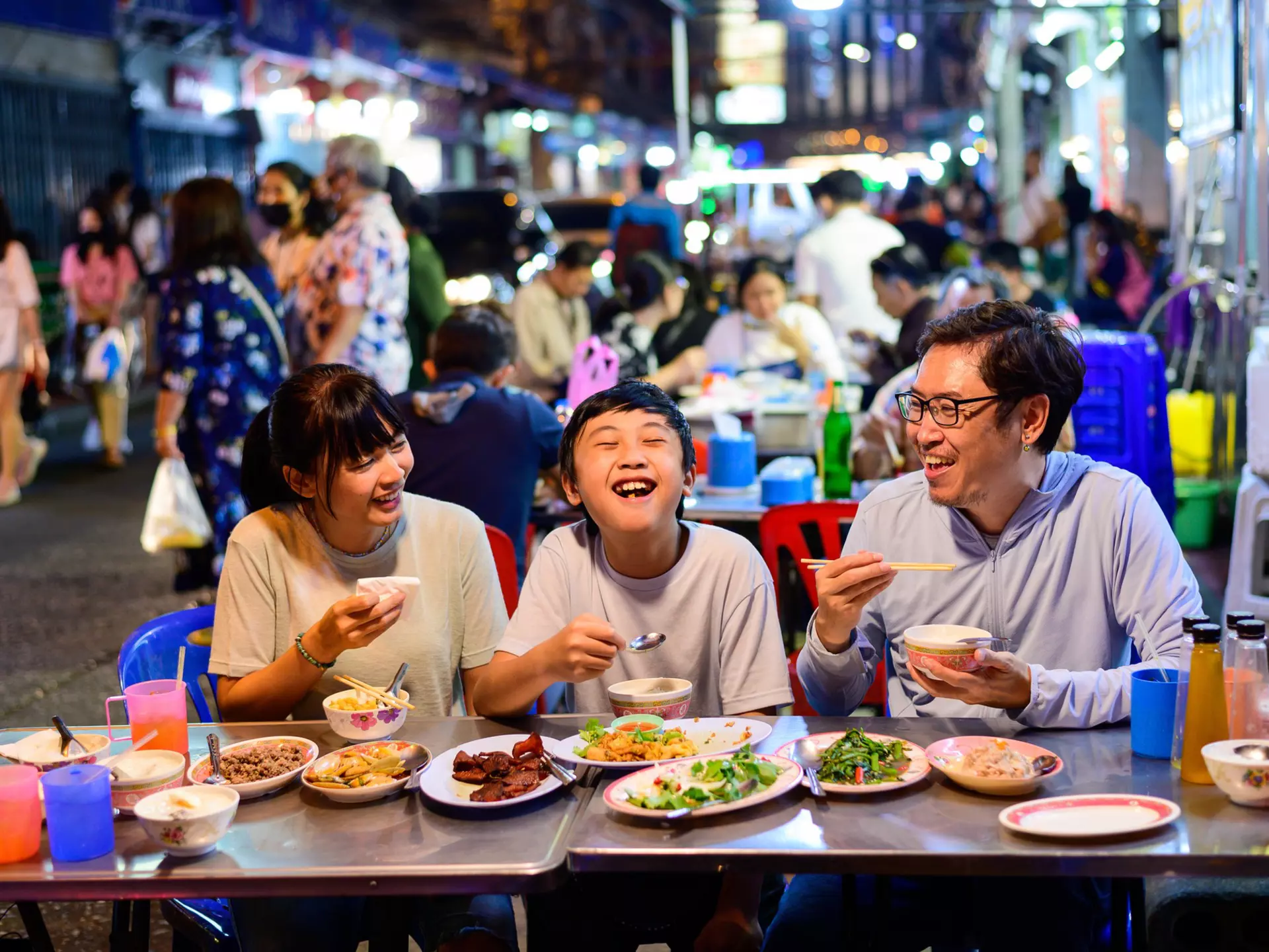 Asian family eating at a street food restaurant with crowd of people behind them