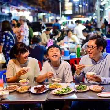 Asian family eating at a street food restaurant with crowd of people behind them