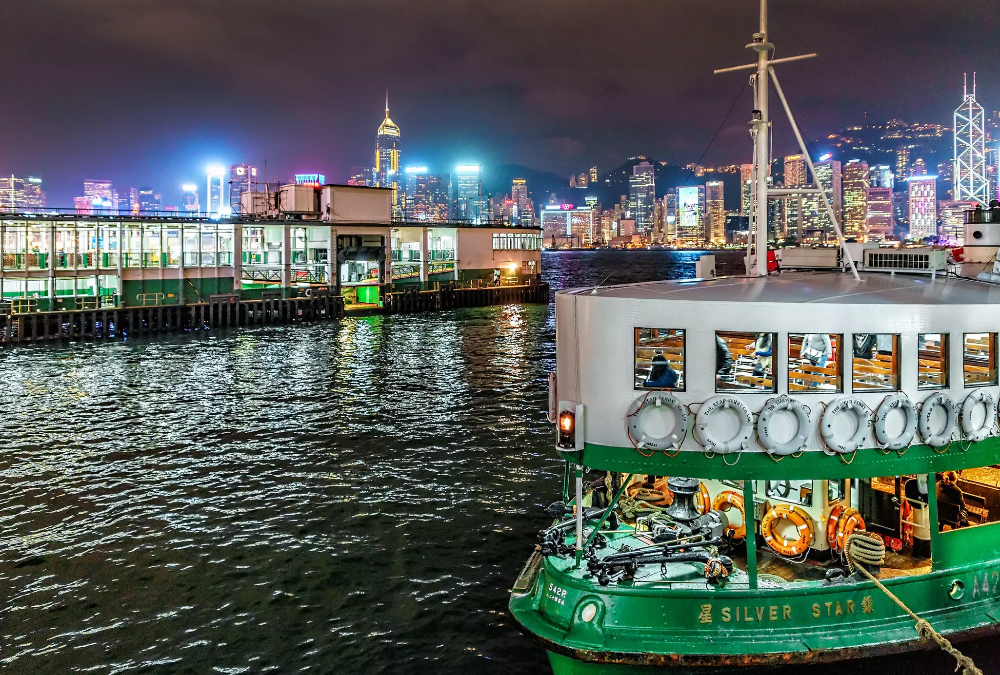 A green and white Star Ferry moored at night in a body of water with Hong Kong skyscrapers in the background